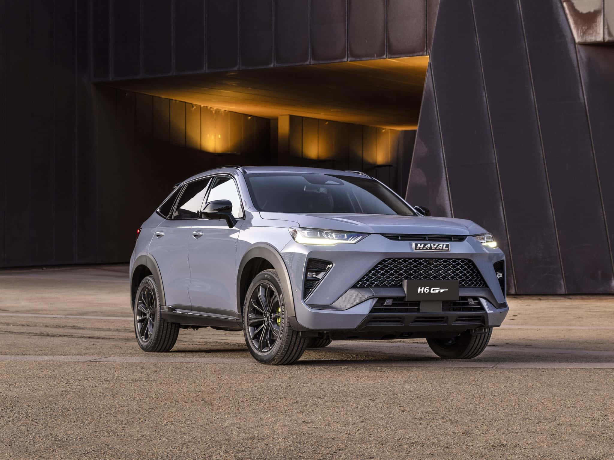 Haval 桌布 壁紙 — 一輛時尚的銀色哈弗H6 GT SUV停放在現代深色建築結構下，配有溫暖的環境照明。