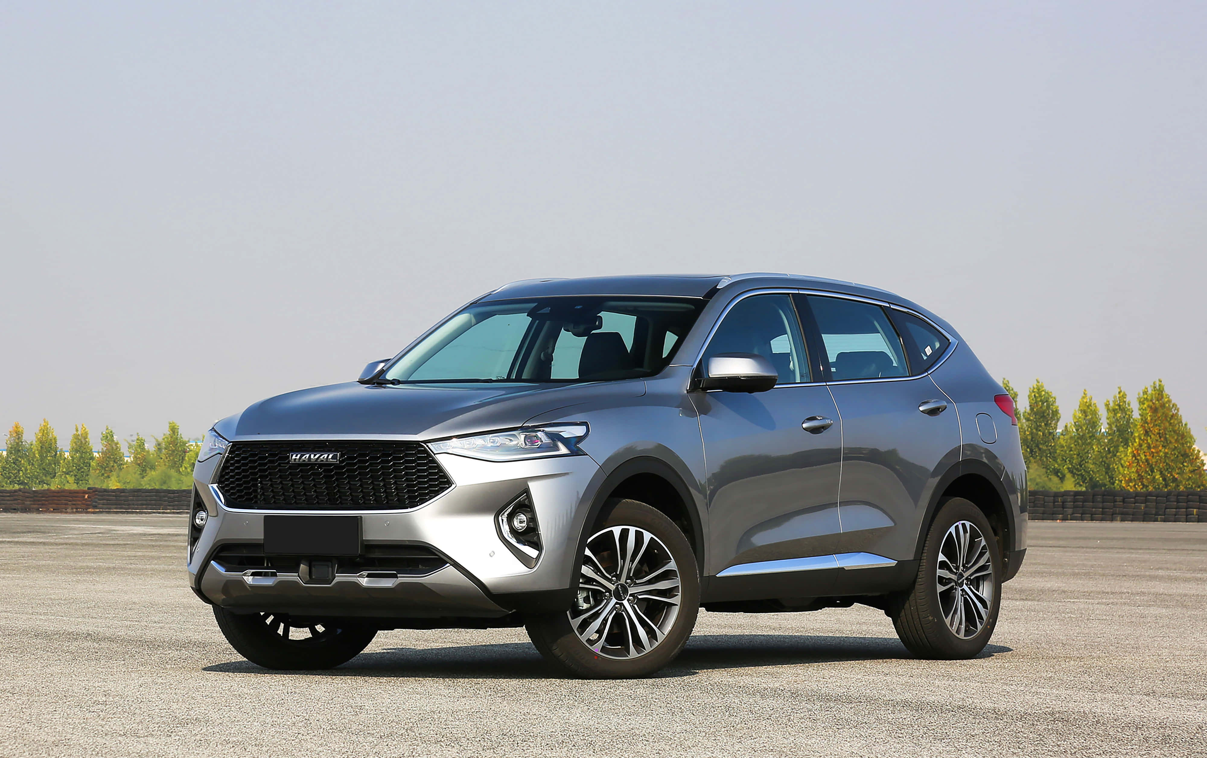 Haval 桌布 壁紙 — 一輛時尚的銀色哈弗SUV停放在開闊的瀝青停車場上，背景有樹木，天空晴朗。