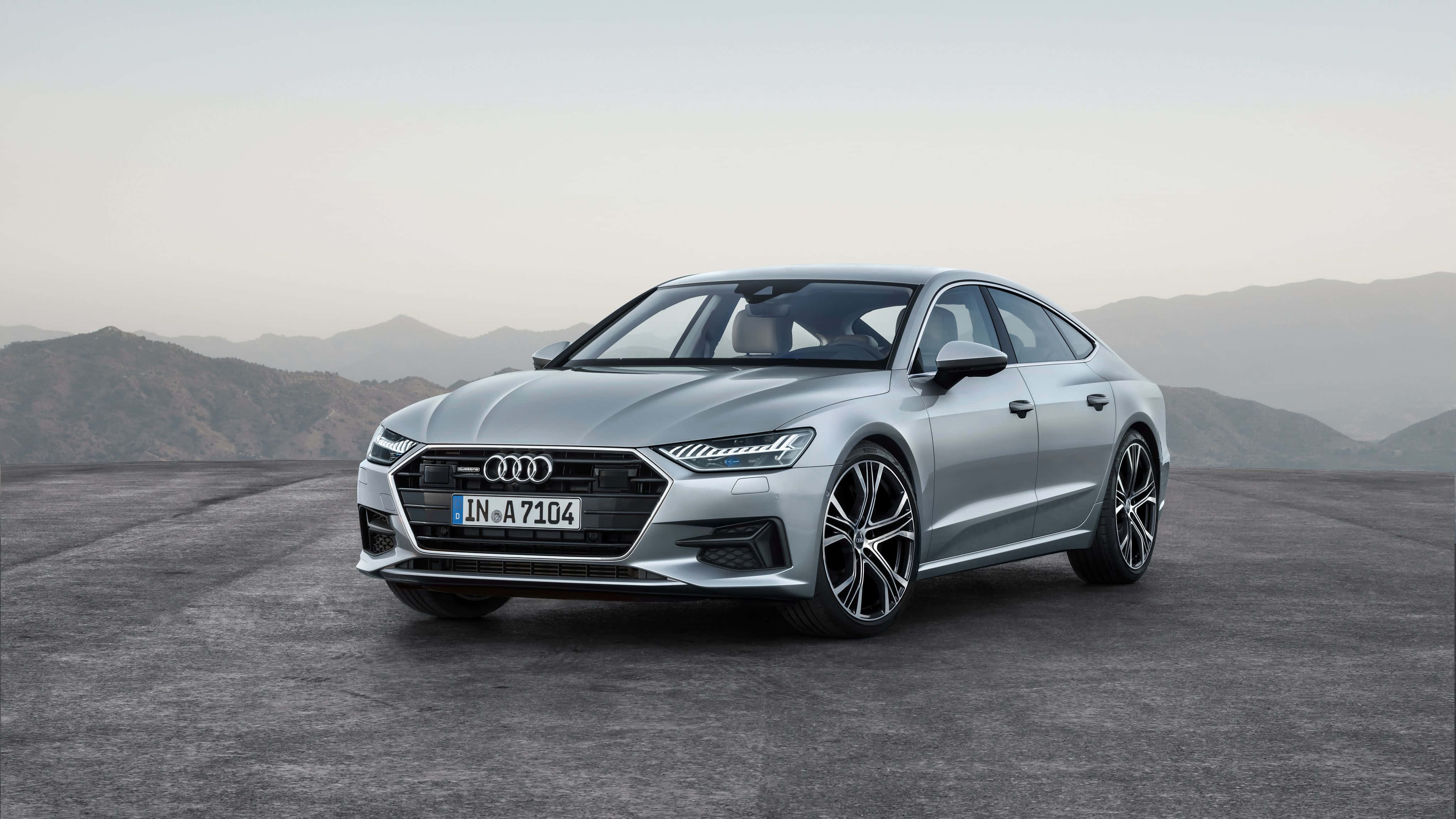 Audi S7 桌布 壁紙 — 一輛時尚的銀色奧迪A7 Sportback停泊在混凝土平台上，背景是朦朧的山巒，在柔和日光下。