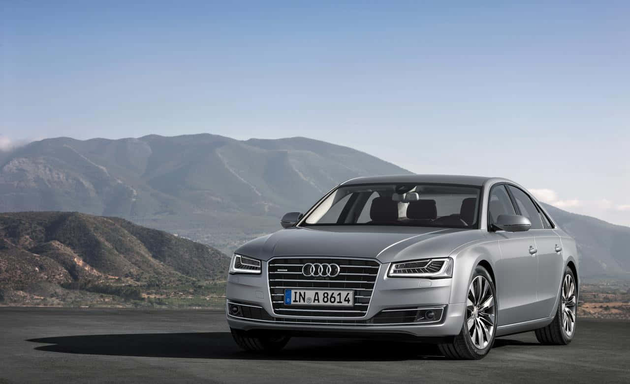 Audi S8 桌布 壁紙 — 一輛時尚的銀色奧迪A8轎車停泊在鋪砌的觀景點上，遠山在晴朗的藍天下。