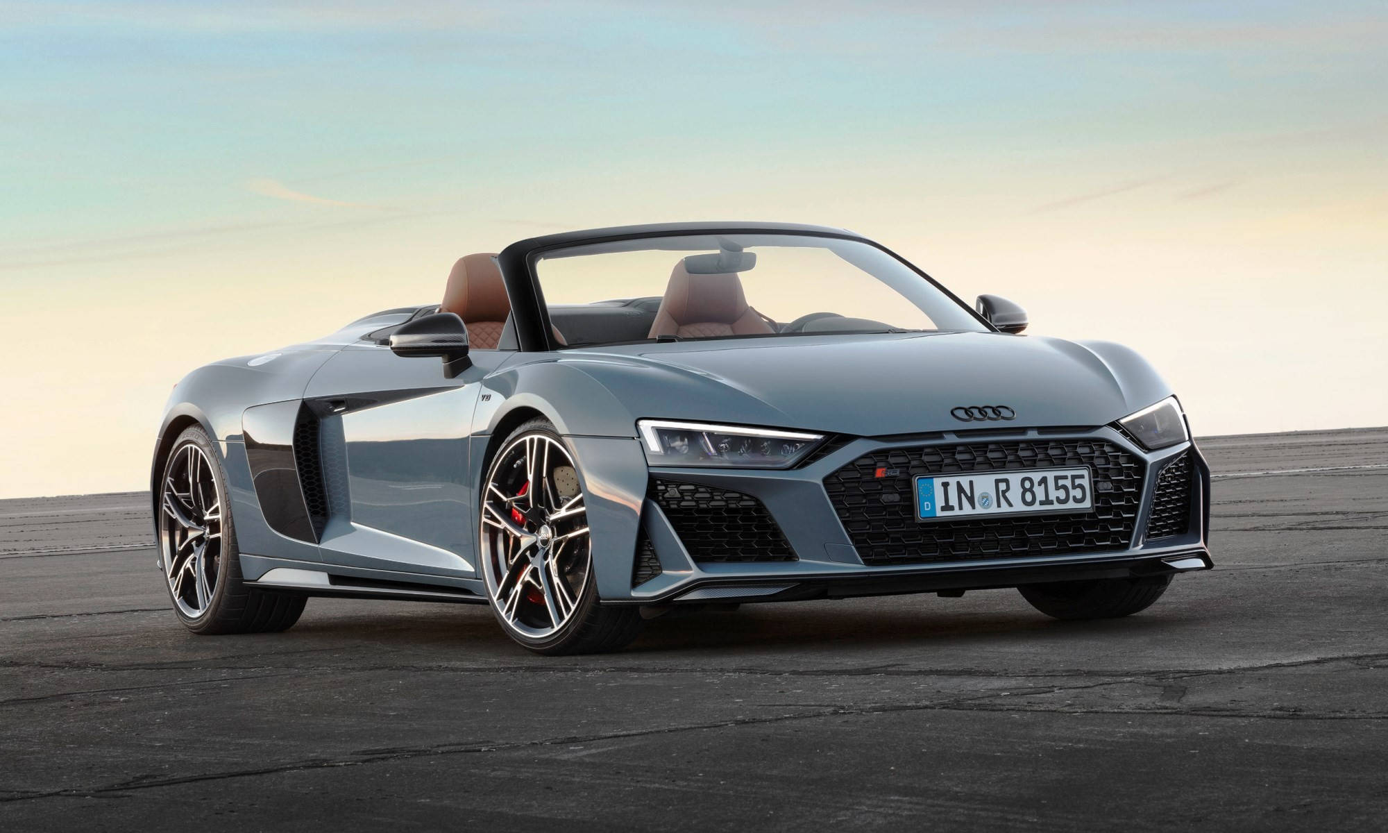 R8 桌布 壁紙 — 一輛時尚的銀色奧迪R8 Spyder敞篷車停放在廣闊的瀝青路面上，背景是日落時分柔和漸變的天空。