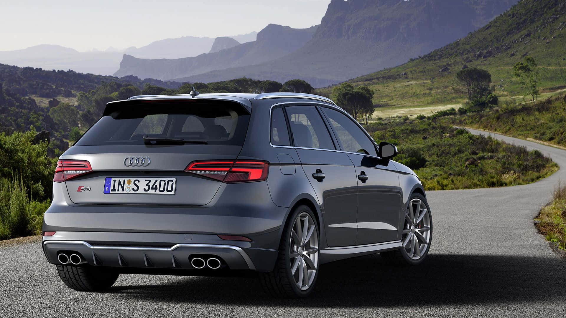Audi S3 桌布 壁紙 — 一輛時尚的銀色奧迪S3旅行車停泊在蜿蜒的山路上，背景是崎嶇的山峰和綠色的山丘。