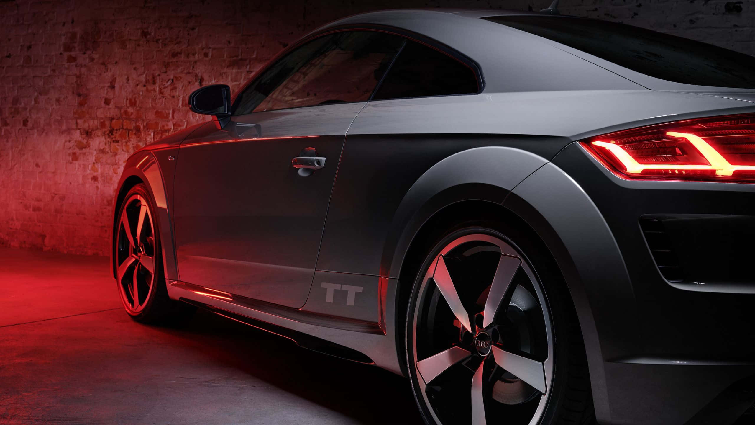 Audi Tt 桌布 壁紙 — 一輛時尚的銀色奧迪TT跑車在戲劇性的紅色燈光下，以紋理磚牆為背景閃耀著光芒。