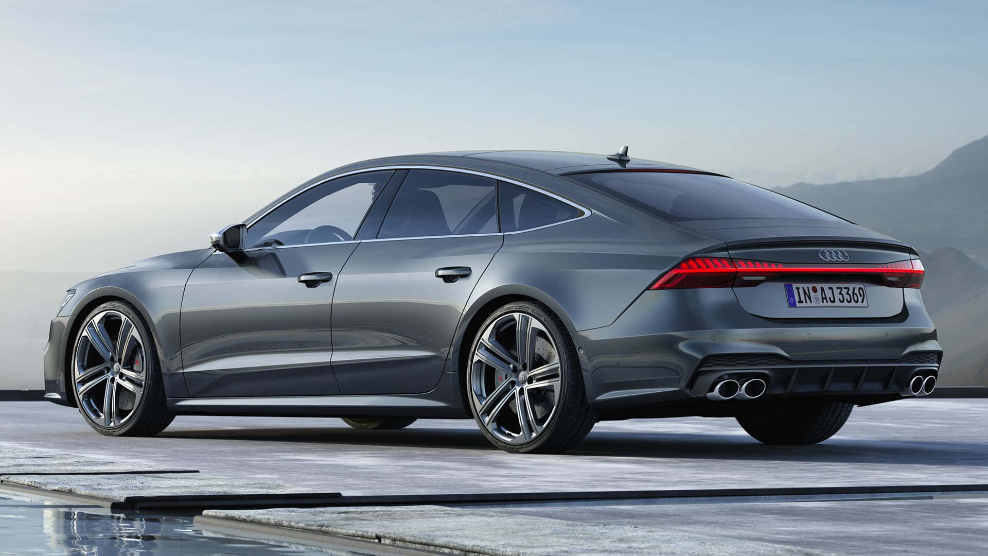 Audi S7 桌布 壁紙 — 一輛時尚的銀色奧迪房車停放在混凝土平台上，背景是山脈和晴朗的天空。