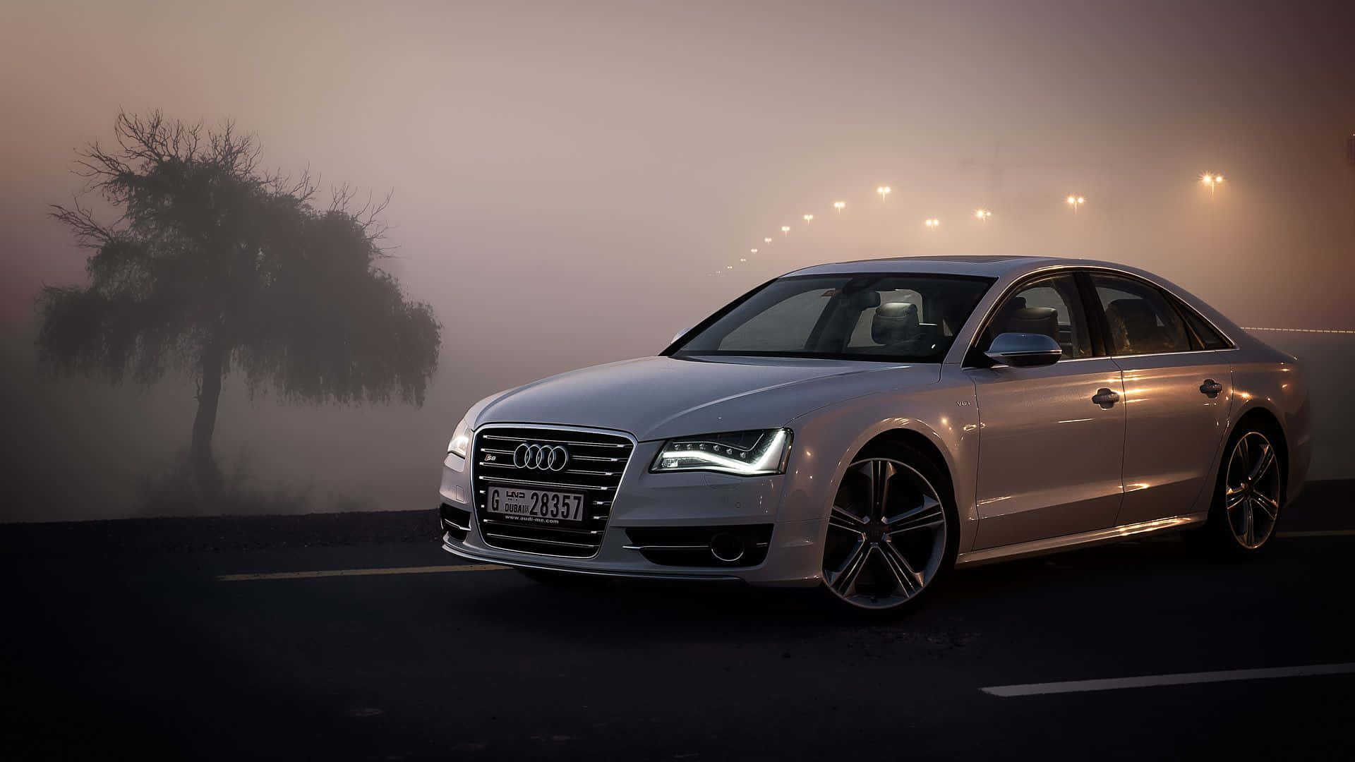 Audi S8 桌布 壁紙 — 一輛時尚的銀色奧迪房車在霧氣瀰漫的道路上，車頭燈照亮著旁邊一棵孤獨的樹，遠處的路燈穿透迷霧。