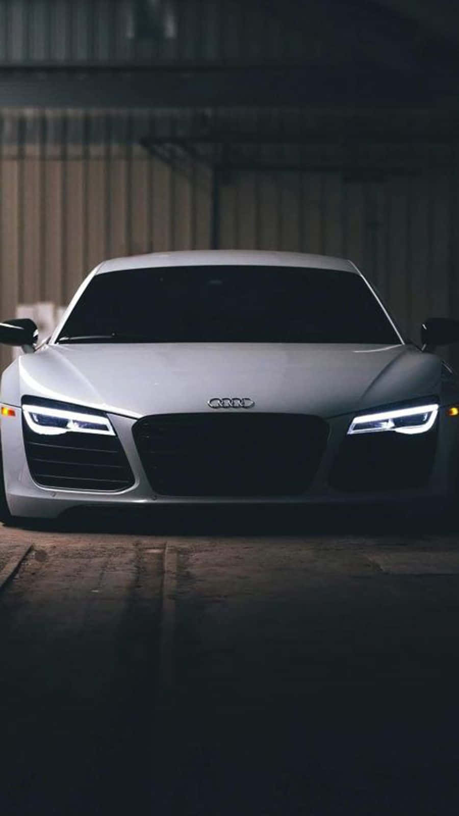 Audi iPhone 桌布 壁紙 — 一輛時尚的銀色奧迪跑車，車頭燈閃爍，在光線昏暗的工業車庫中凝視前方。