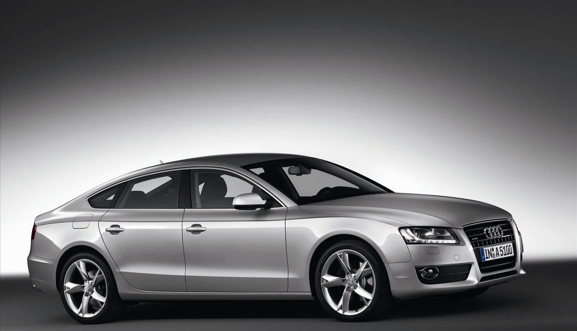 Audi A5 桌布 壁紙 — 一輛時尚的銀色奧迪轎車在攝影棚燈光下，映襯著漸變灰色背景閃閃發光。