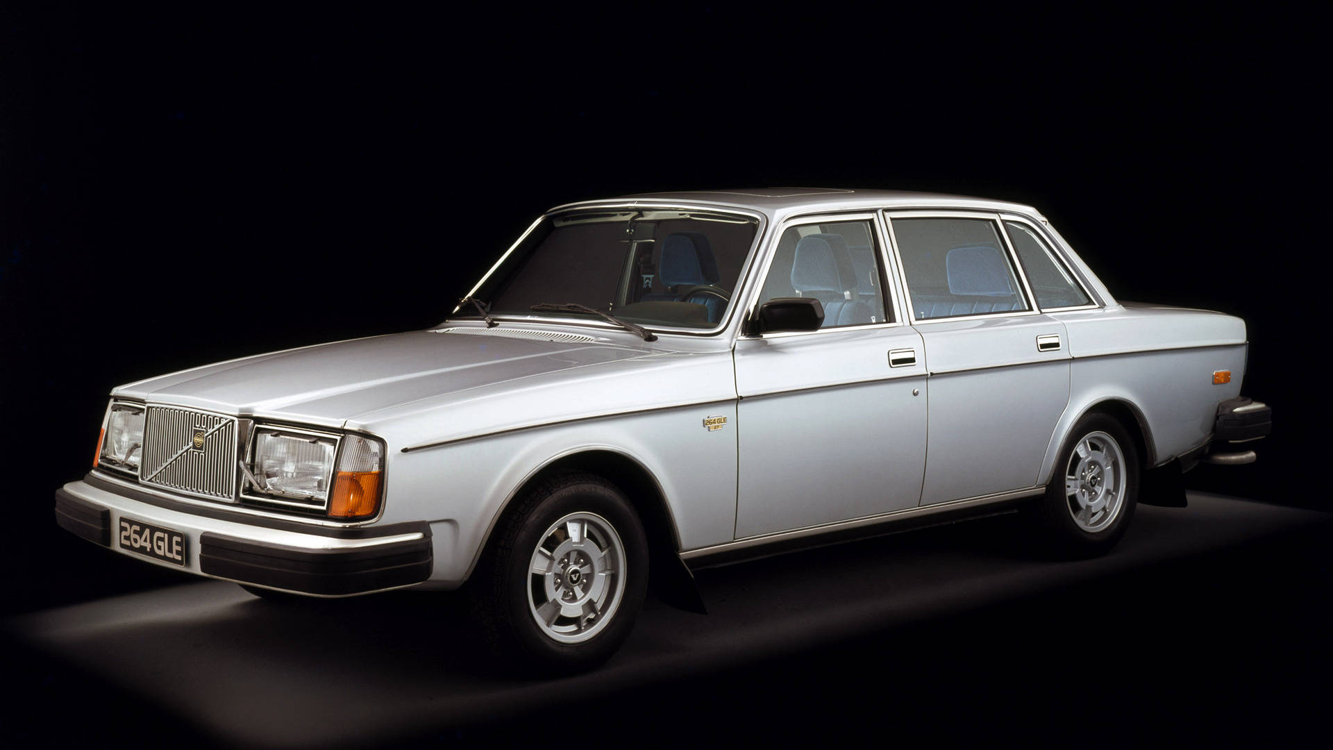 volvo iPhone 桌布 壁紙 — 一輛時尚的銀色富豪 264 GLE 轎車在黑色背景的戲劇性攝影棚照中展示，配有聚光燈。