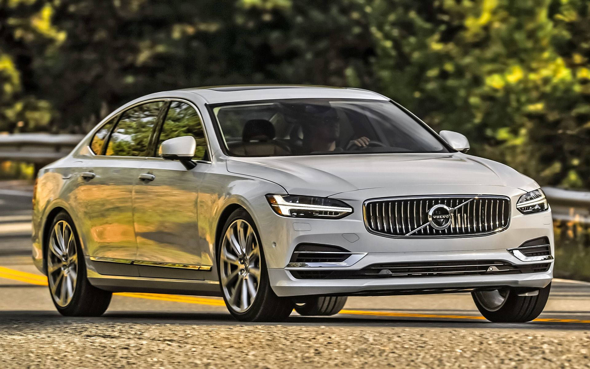 Volvo 桌布 壁紙 — 一輛時尚的銀色富豪S90轎車沿著陽光普照、綠樹成蔭的道路行駛。