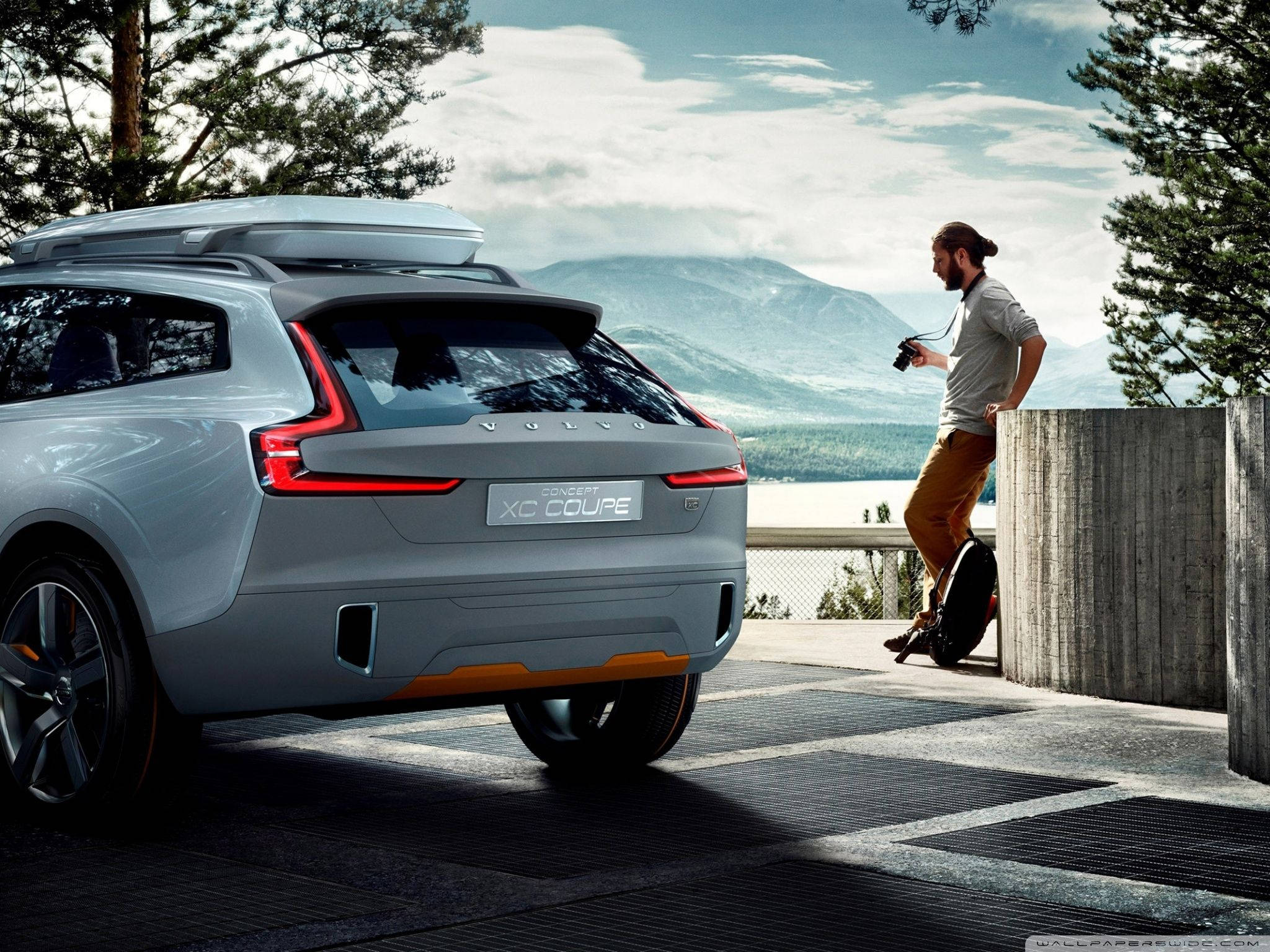 Volvo 桌布 壁紙 — 一輛時尚的銀色富豪XC Coupe概念車停在山頂觀景點，一名男子拿著相機靠在混凝土護欄上。