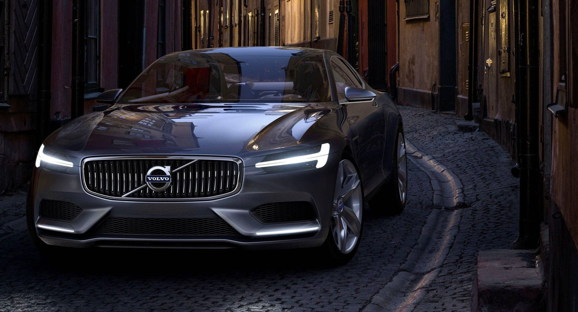 Volvo 桌布 壁紙 — 一輛時尚的銀色富豪概念車在黃昏時分沿著歷史悠久的磚砌建築之間的狹窄鵝卵石小巷滑行。