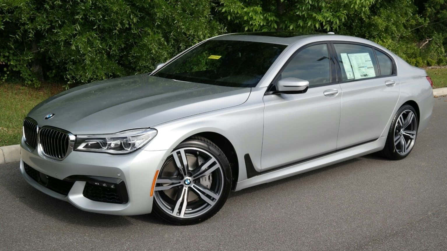 Bmw 7 Series 桌布 壁紙 — 一輛時尚的銀色寶馬7系列轎車停在瀝青路面上，背景是茂密的綠色灌木叢。