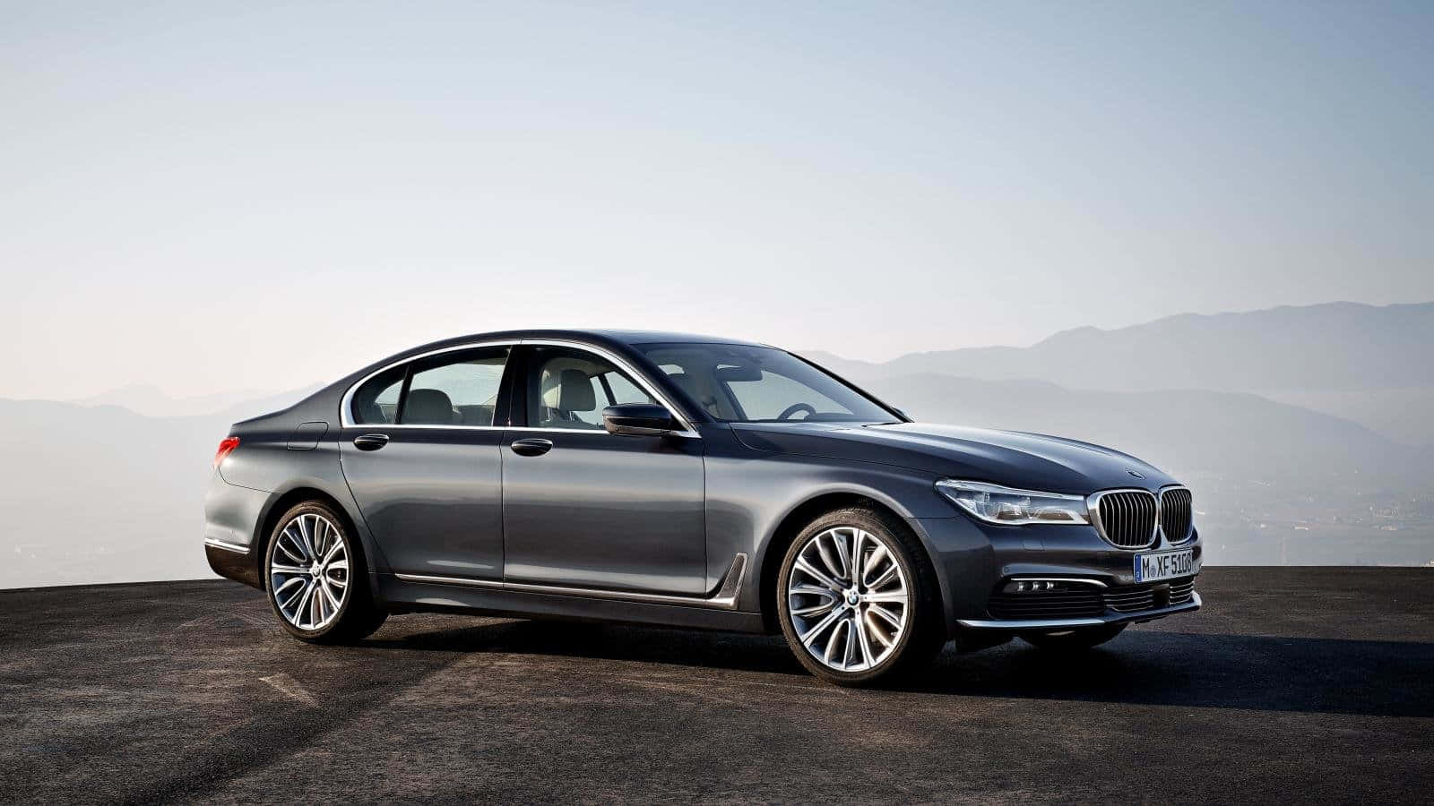Bmw 7 Series 桌布 壁紙 — 一輛時尚的銀色寶馬7系列轎車停泊在懸崖上，俯瞰著朦朧天空下的遠山。
