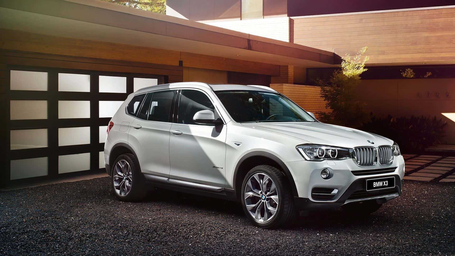 Bmw X3 桌布 壁紙 — 一輛時尚的銀色寶馬X3 SUV停泊在碎石路上，前面是一間設有玻璃車庫門的現代木屋。