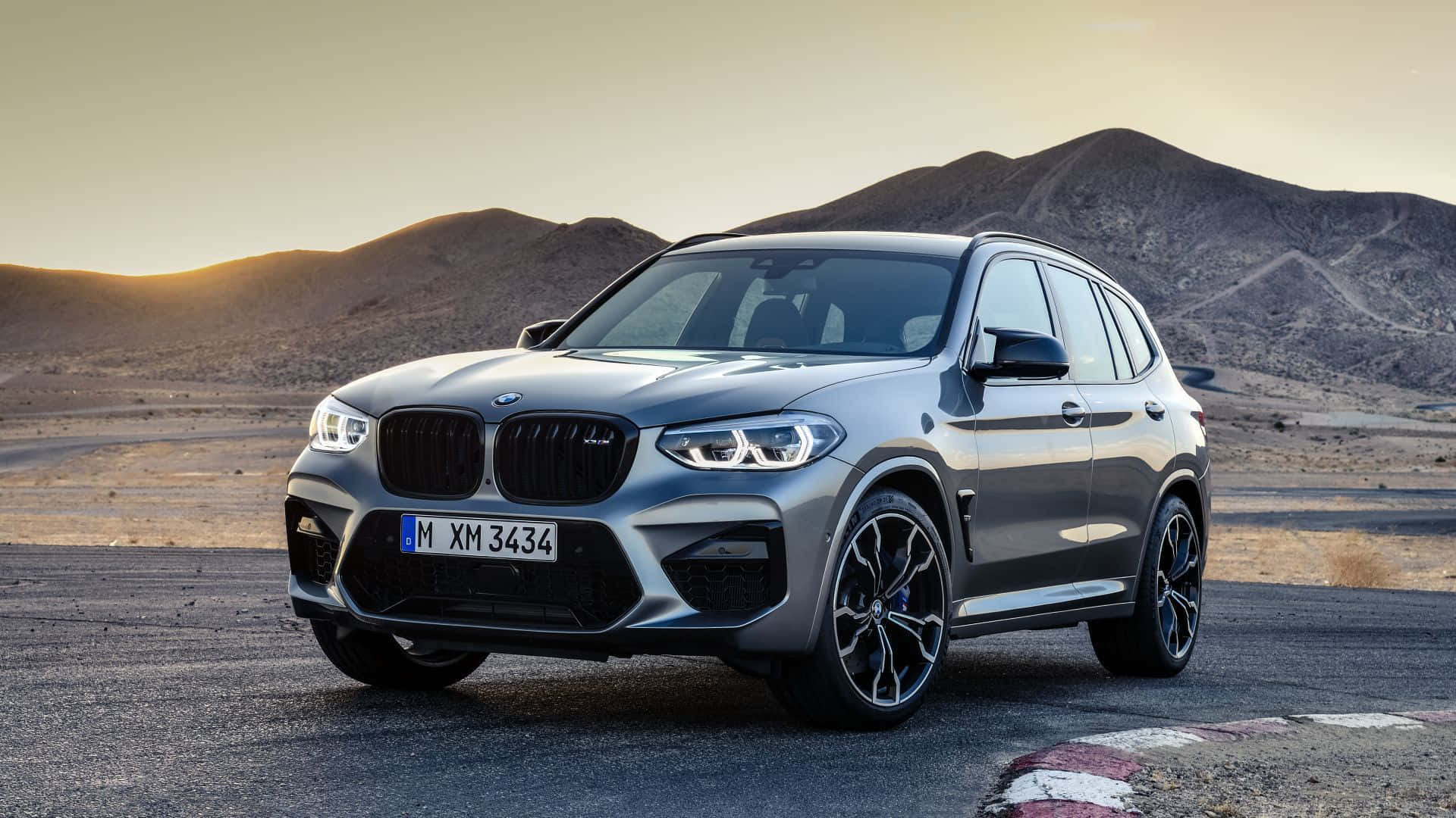 Bmw X3 桌布 壁紙 — 一輛時尚的銀色寶馬XM SUV停泊在沙漠賽道上，背景是黃金時段的山脈。
