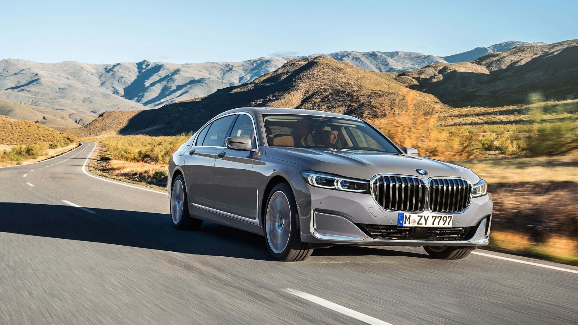 Bmw 7 Series 桌布 壁紙 — 一輛時尚的銀色寶馬轎車在晴朗藍天下沿著蜿蜒的山路行駛。