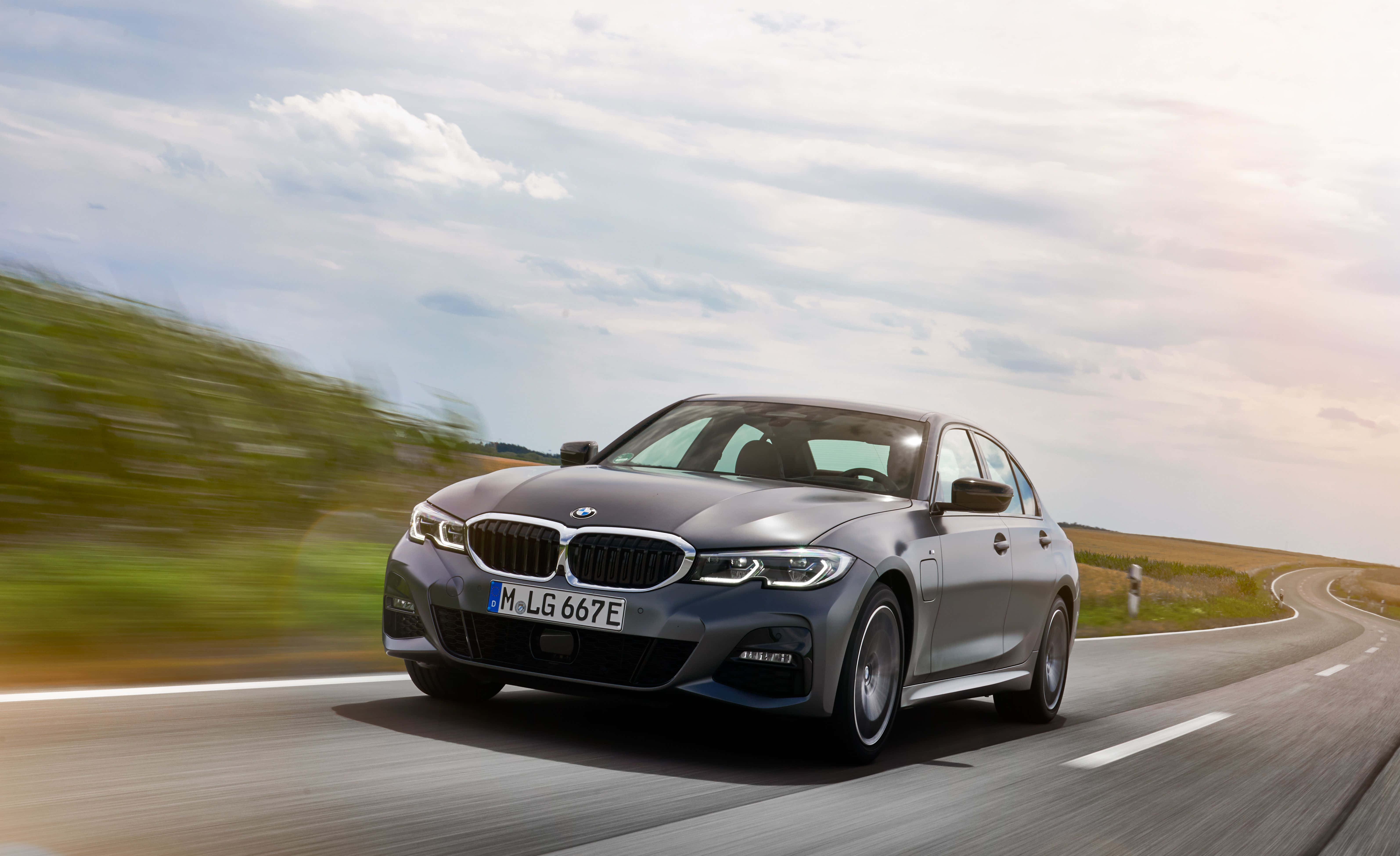 Bmw 3 Series 桌布 壁紙 — 一輛時尚的銀色寶馬轎車在部分多雲的天空下，沿著蜿蜒的鄉村道路疾馳，周圍環境帶有動態模糊效果。