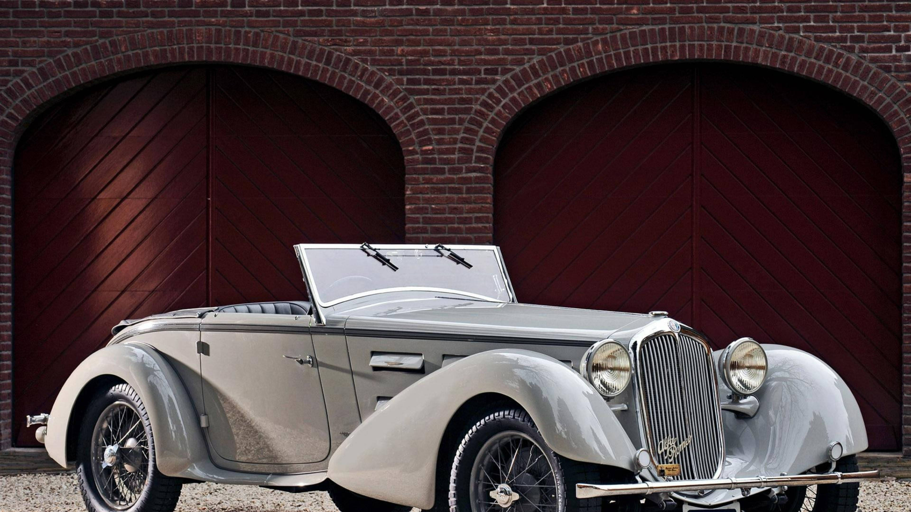 Alfa Romeo 桌布 壁紙 — 一輛時尚的銀色復古敞篷車停在磚砌建築的兩個拱形紅色木車庫門前。