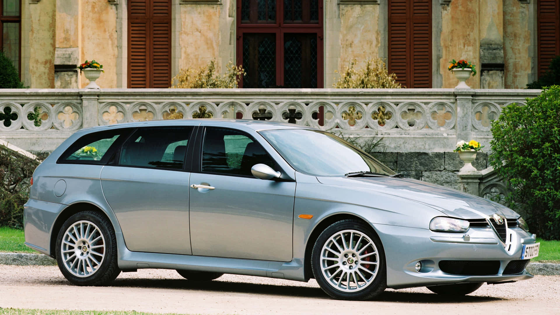 Alfa Romeo 156 桌布 壁紙 — 一輛時尚的銀色愛快羅密歐156旅行車停在碎石路上，前面是一座宏偉的石砌別墅，帶有華麗的欄杆和盆栽花卉。