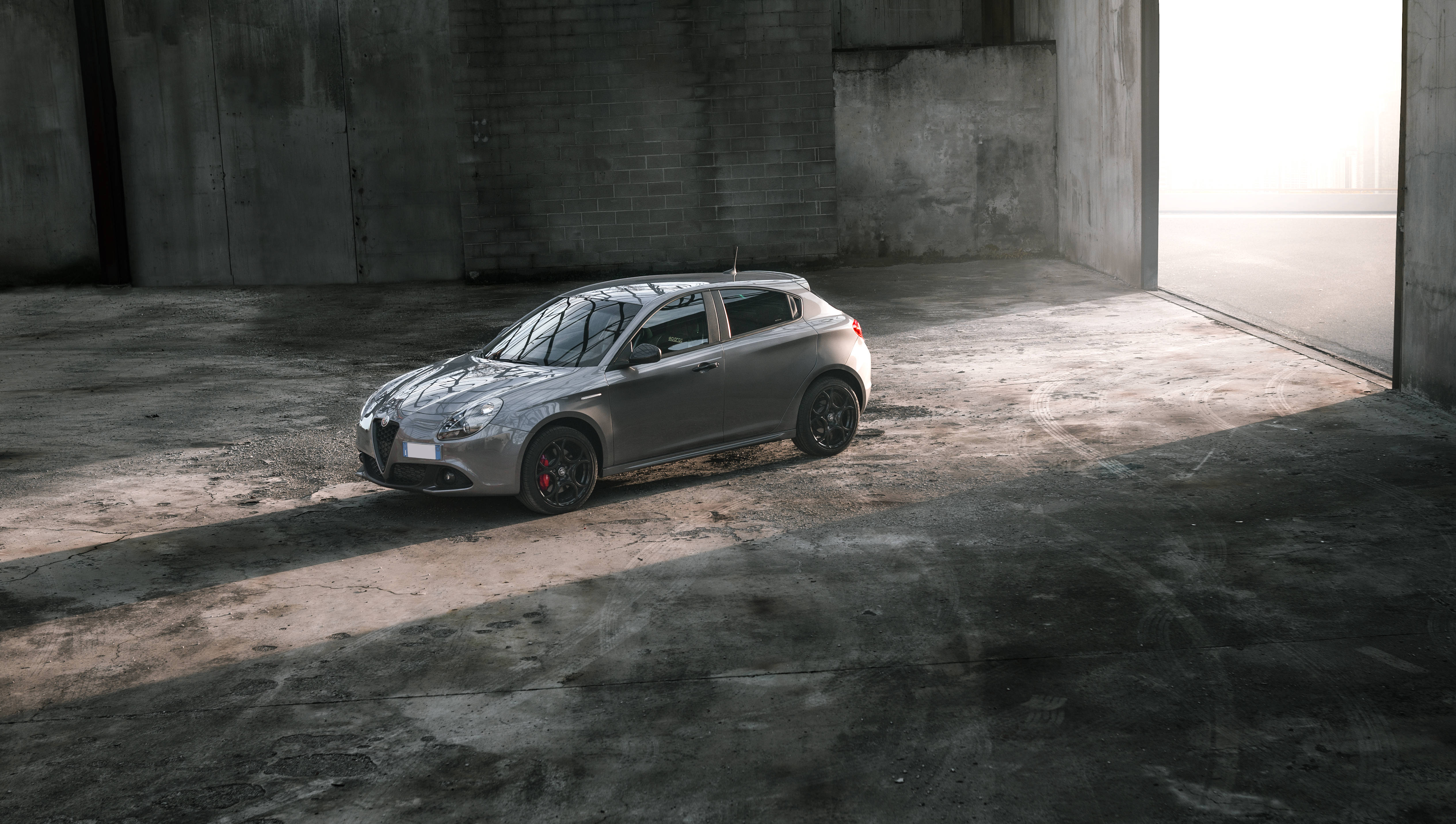 Alfa Romeo 桌布 壁紙 — 一輛時尚的銀色愛快羅密歐Giulietta停放在陽光普照的混凝土倉庫中，帶有戲劇性的陰影。