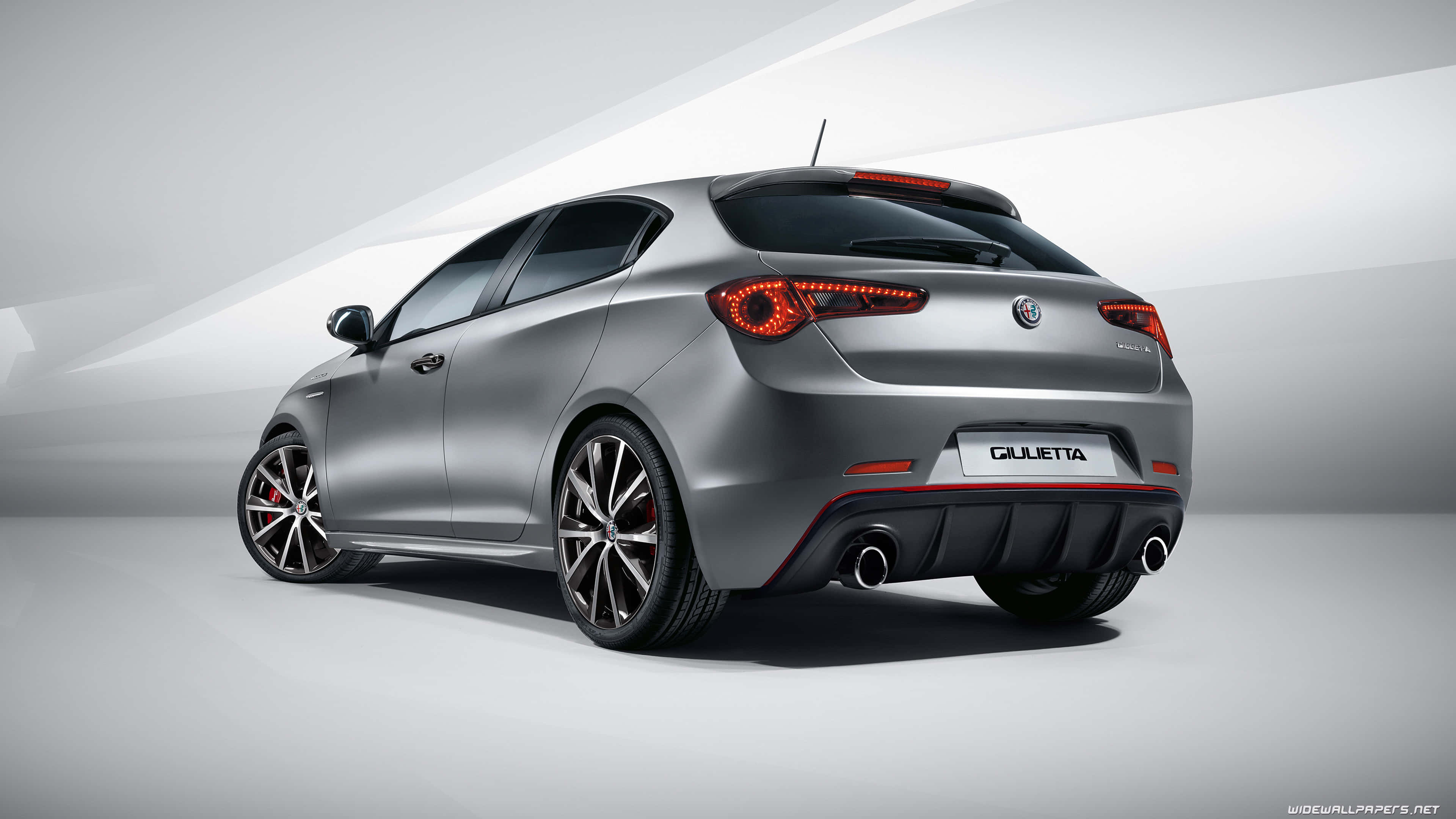 Alfa Romeo Giulietta 桌布 壁紙 — 一輛時尚的銀色愛快羅密歐Giulietta掀背車，從後方四分之三角度在簡約工作室中以戲劇性燈光展示。