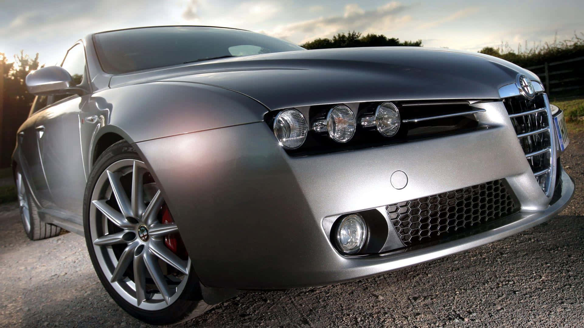 Alfa Romeo 159 桌布 壁紙 — 一輛時尚的銀色愛快羅密歐跑車在碎石路上閃耀著金色的夕陽光芒。