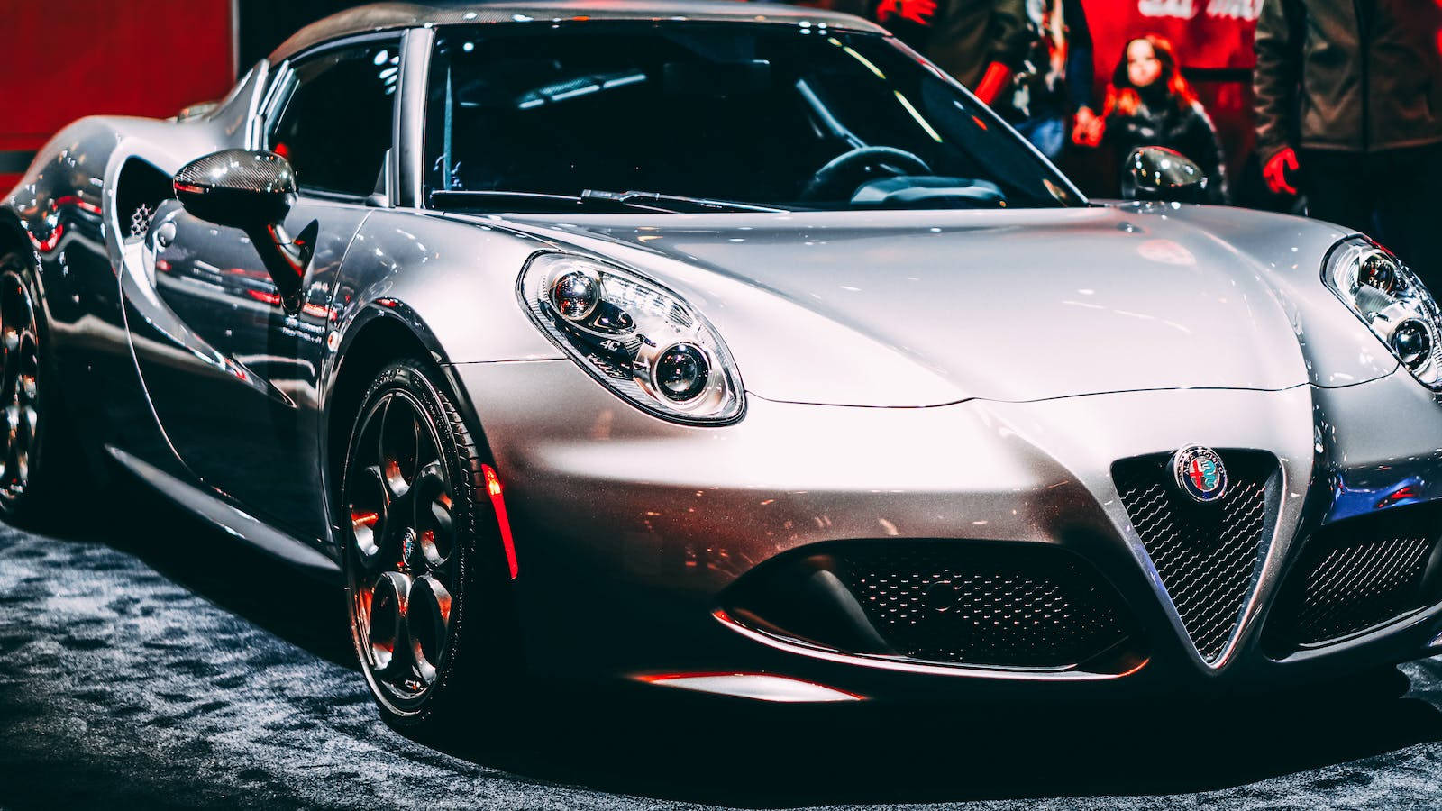 Luxury 桌布 壁紙 — 一輛時尚的銀色愛快羅密歐跑車在車展的明亮燈光下閃閃發光，背景是模糊的觀眾。