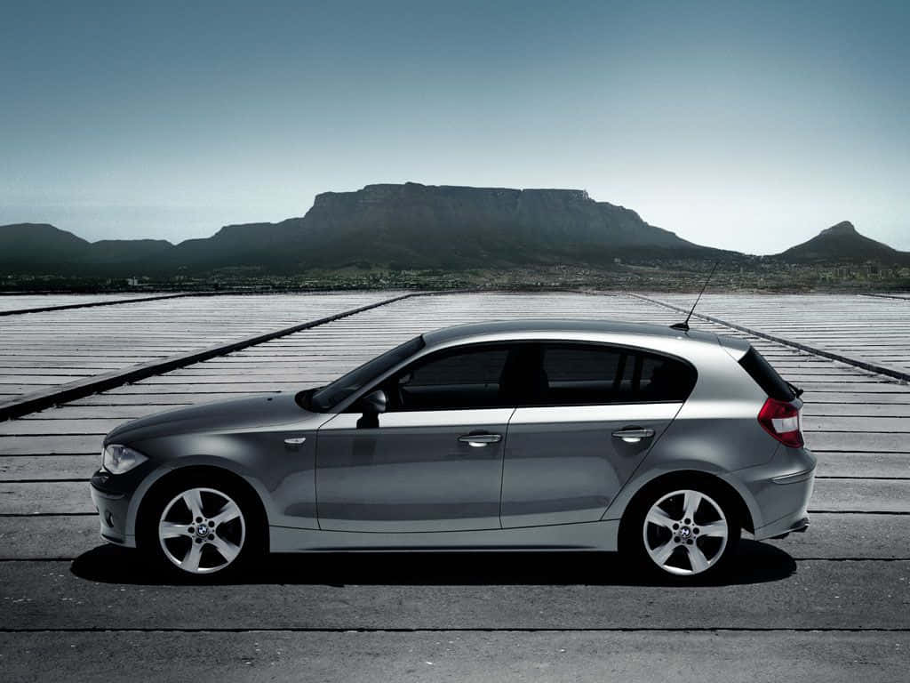 Bmw 1 Series 桌布 壁紙 — 一輛時尚的銀色掀背車停泊在木製碼頭上，背景是晴朗天空下的桌山。