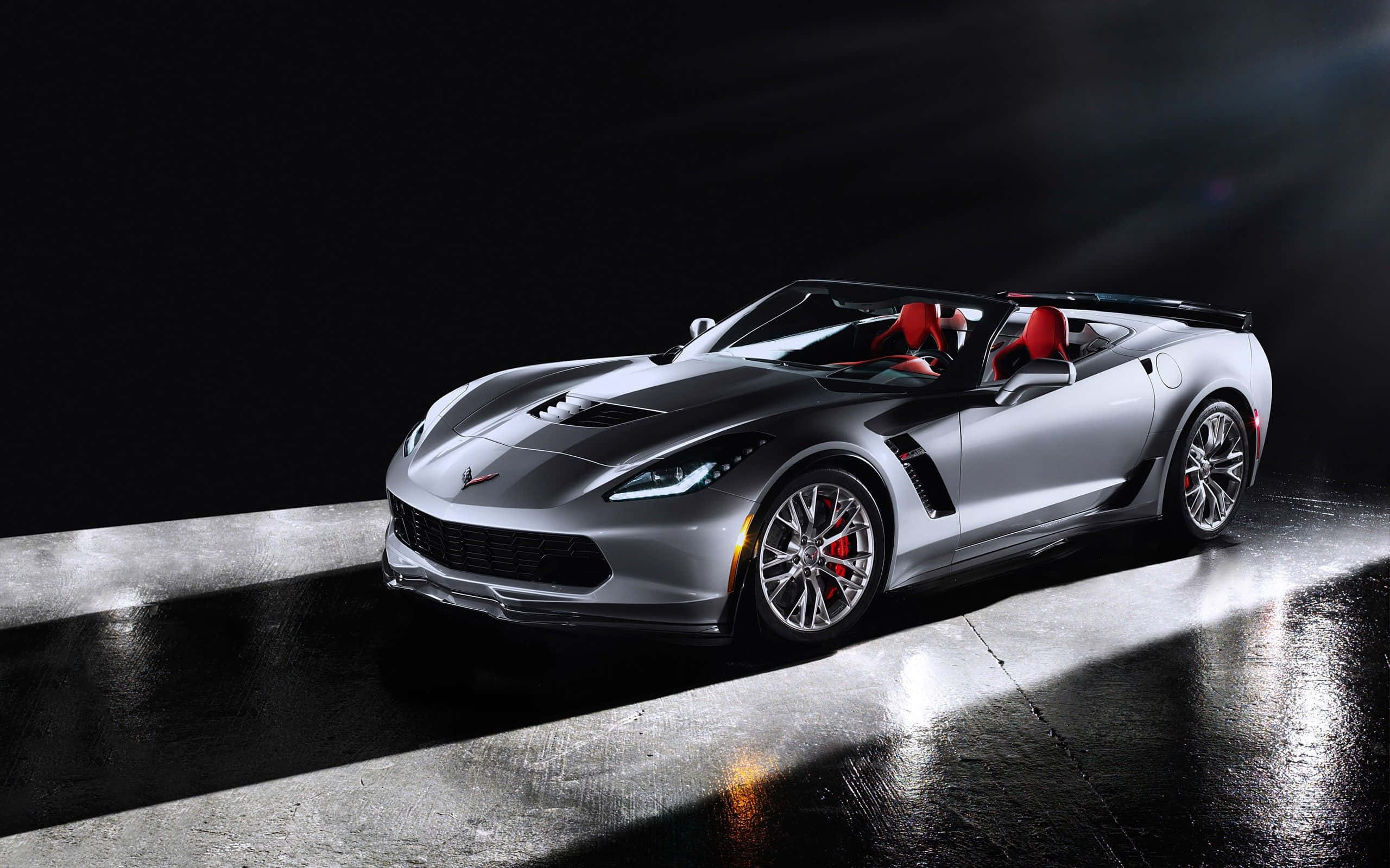 Chevrolet Corvette Z06 桌布 壁紙 — 一輛時尚的銀色敞篷跑車，紅色內裝，在潮濕的混凝土地板上，在戲劇性的聚光燈下閃閃發光。