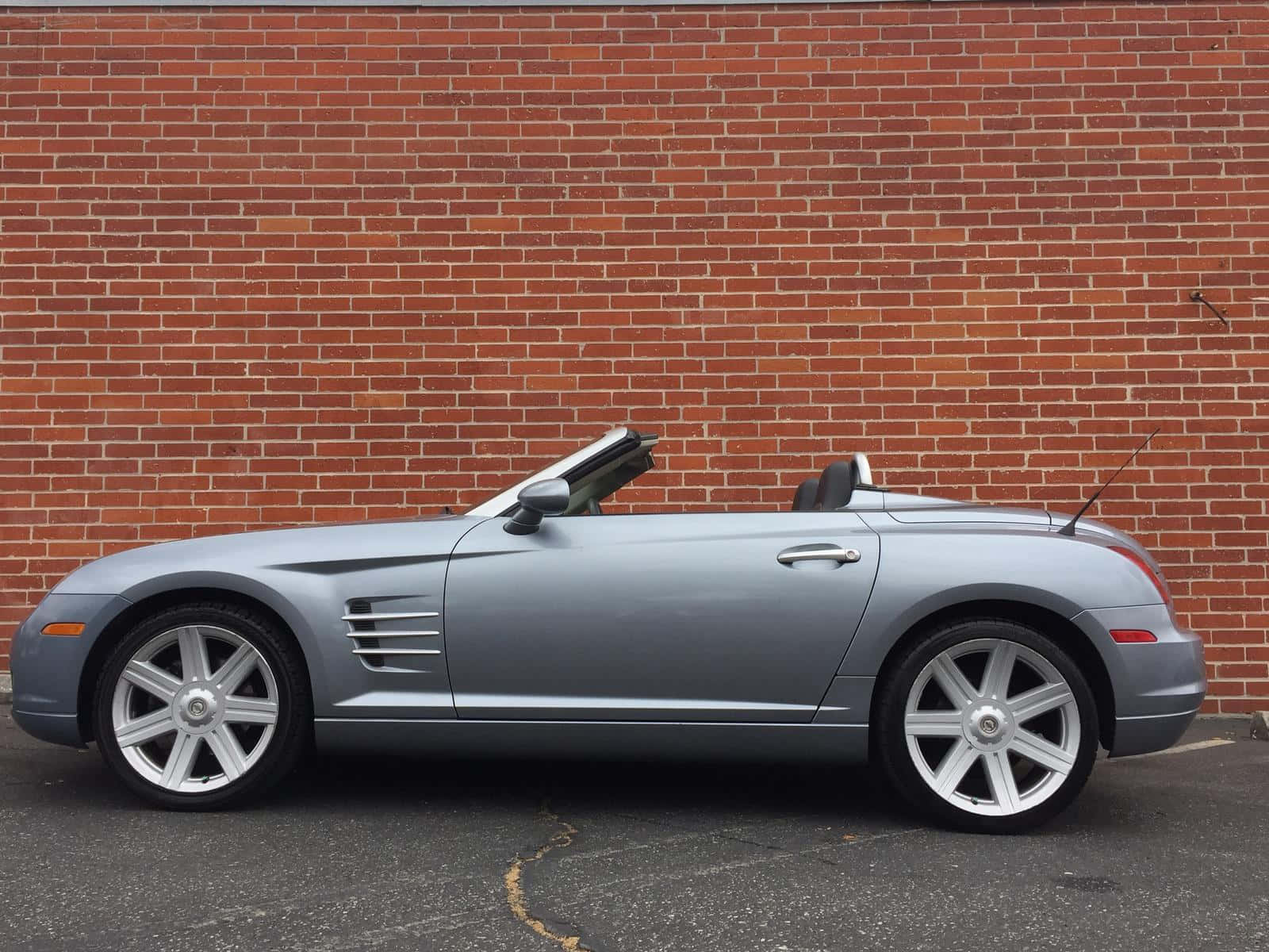 Chrysler Crossfire 桌布 壁紙 — 一輛時尚的銀色敞篷跑車停在紅磚牆前的柏油路面上。