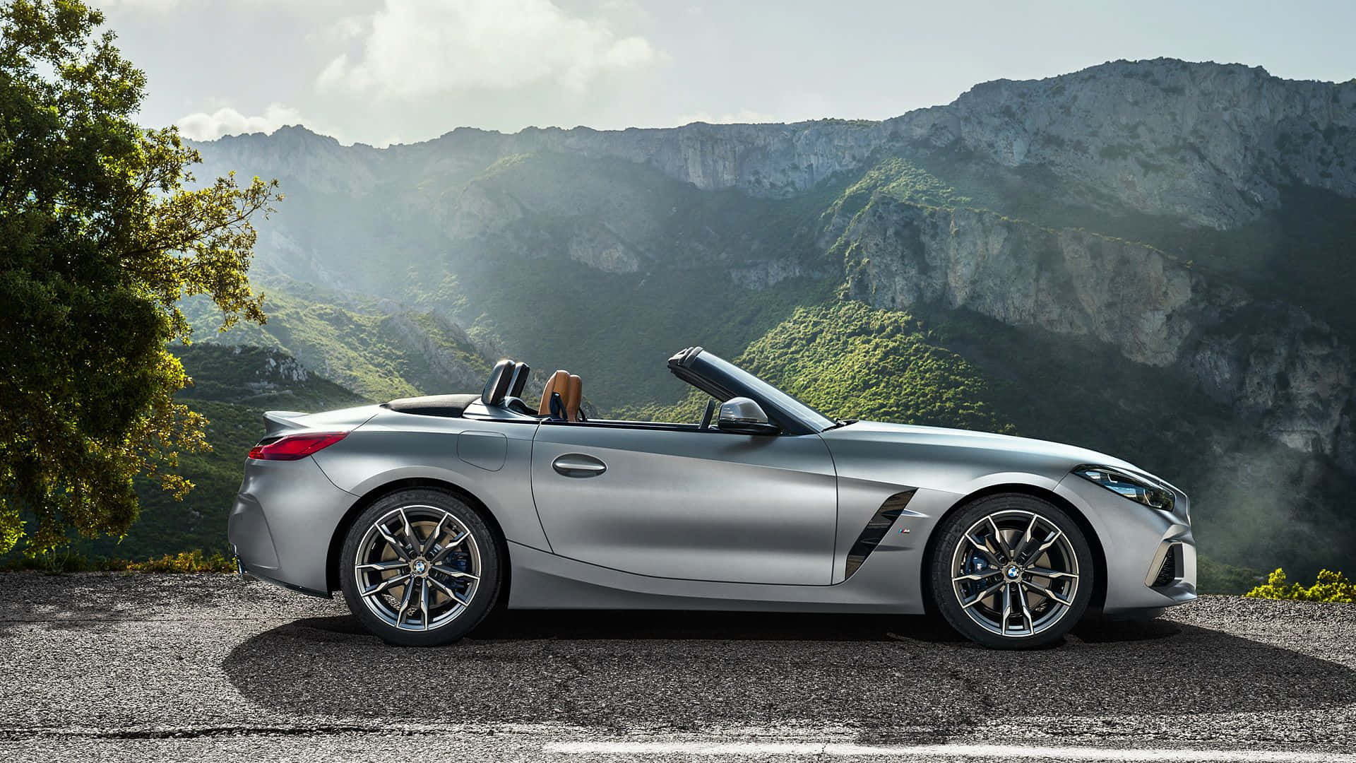 Bmw Z4 桌布 壁紙 — 一輛時尚的銀色敞篷跑車停泊在山路上，背景是茂密的綠色山丘和岩石山峰。