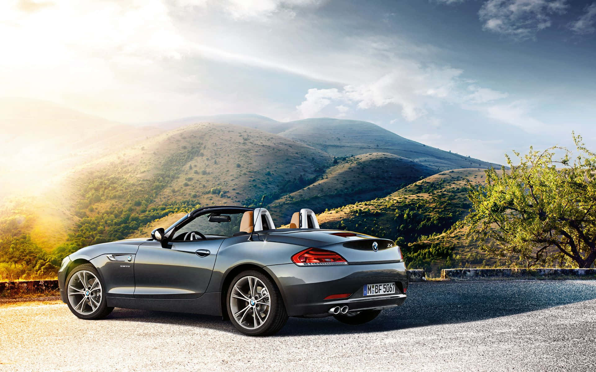 Bmw Z4 桌布 壁紙 — 一輛時尚的銀色敞篷跑車停泊在碎石路上，背景是陽光普照的起伏山丘和零星樹木。