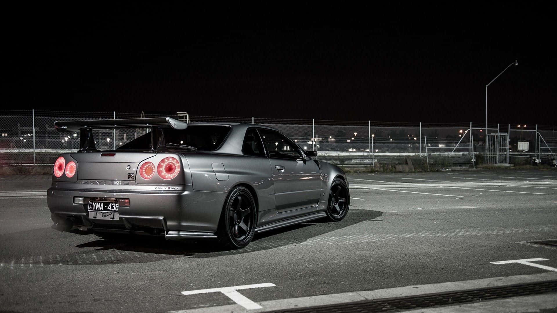 Nissan Skyline 桌布 壁紙 — 一輛時尚的銀色日產GT-R在夜間停放在空地上，紅色尾燈閃爍，天空漆黑。