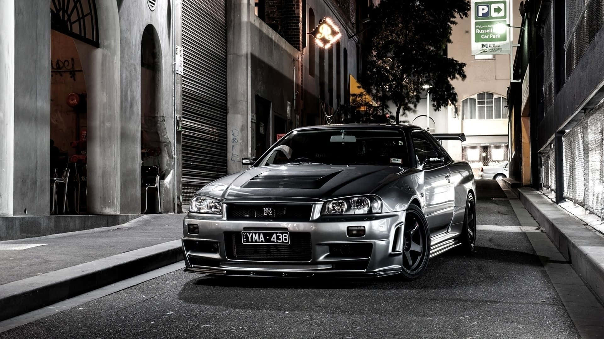 桌布 壁紙 — 一輛時尚的銀色日產Skyline R34跑車在夜間停放在狹窄的城市小巷中，帶有戲劇性的燈光。