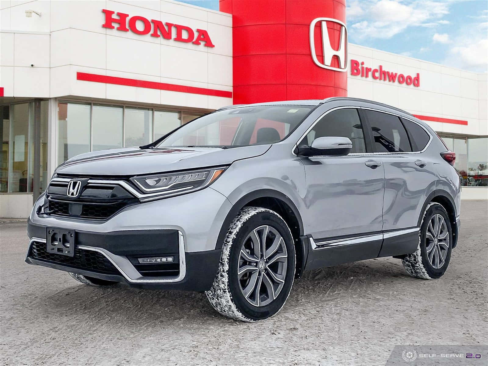 Honda Cr-v 桌布 壁紙 — 一輛時尚的銀色本田 CR-V SUV 停放在現代化的本田經銷商前，店面採用紅白品牌標誌，背景是清澈的藍天。