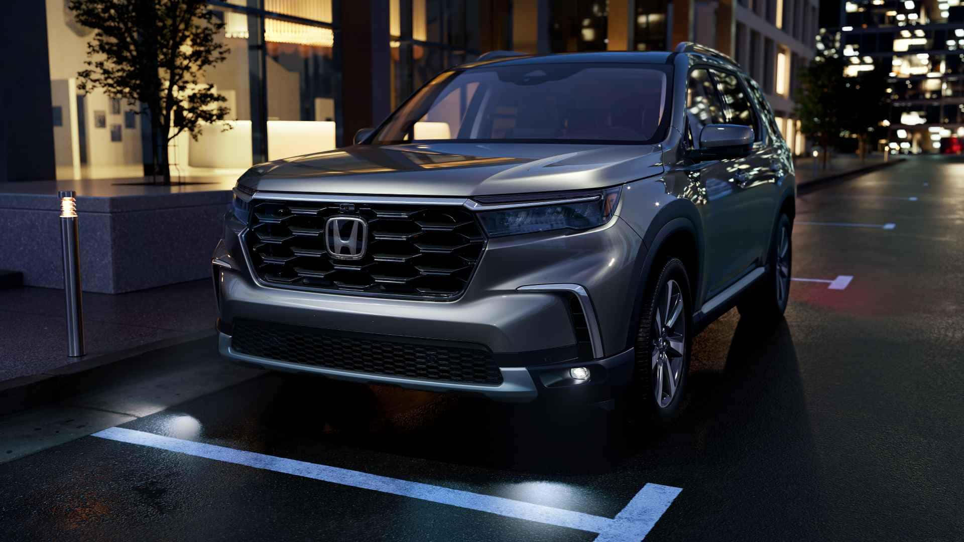 Honda Pilot 桌布 壁紙 — 一輛時尚的銀色本田SUV在夜間停泊於城市街道，反射濕漉漉的路面和閃爍的建築燈光。