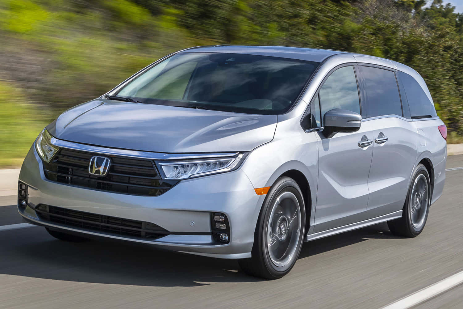 Honda Odyssey 桌布 壁紙 — 一輛時尚的銀色本田小型貨車在陽光明媚的道路上行駛，模糊的綠色樹葉飛馳而過。