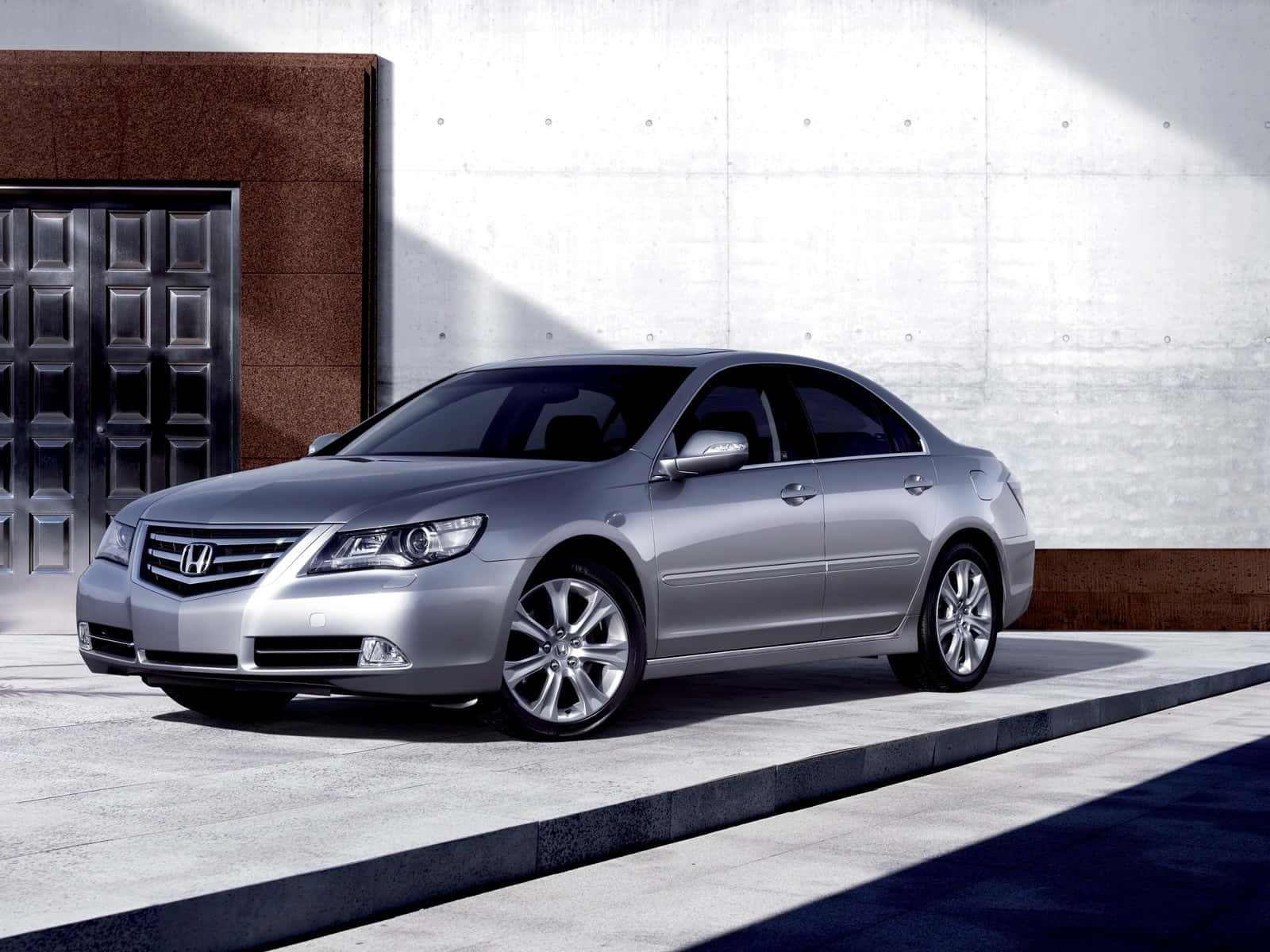 Honda Legend 桌布 壁紙 — 一輛時尚的銀色本田雅閣轎車停放在現代建築旁的混凝土人行道上，建築有深色門和紋理牆壁。