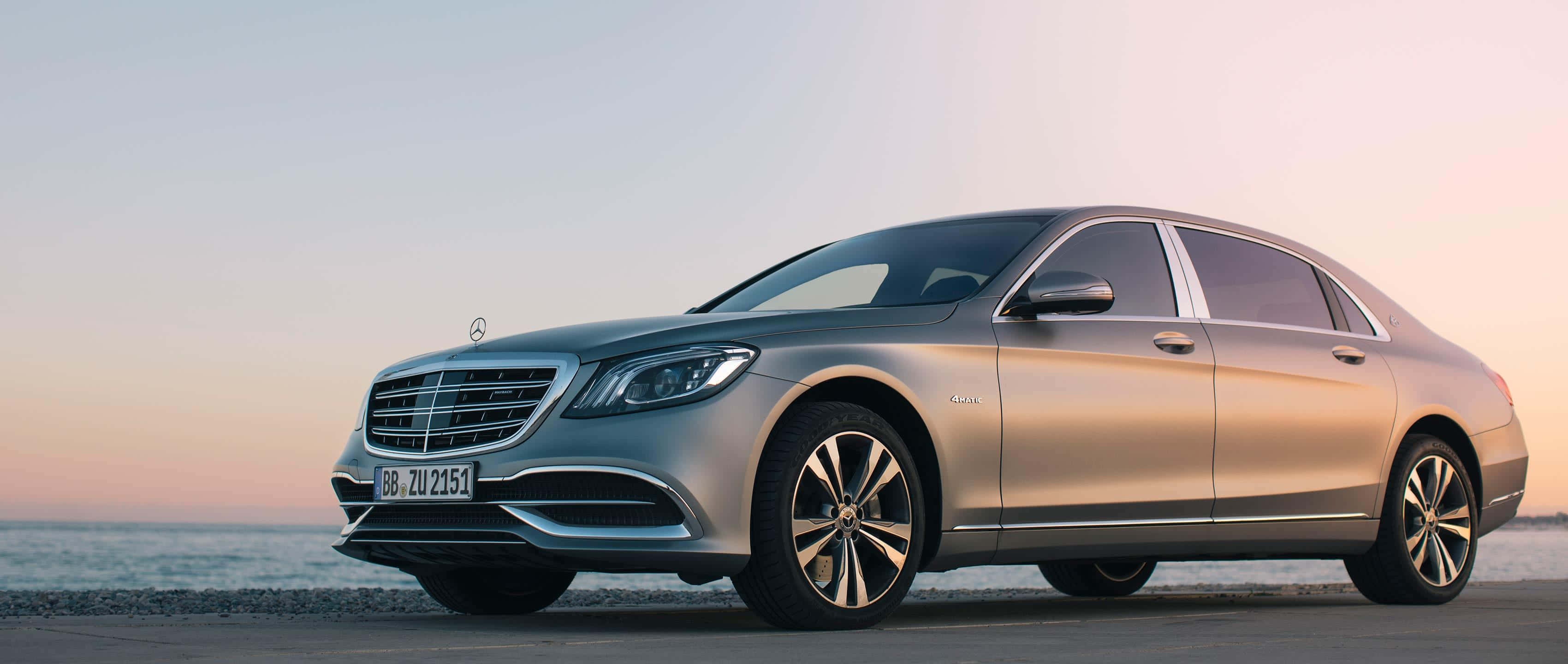 Maybach 桌布 壁紙 — 一輛時尚的銀色梅賽德斯-奔馳S級轎車停在日落時分的海岸公路上，背後是平靜的海水。