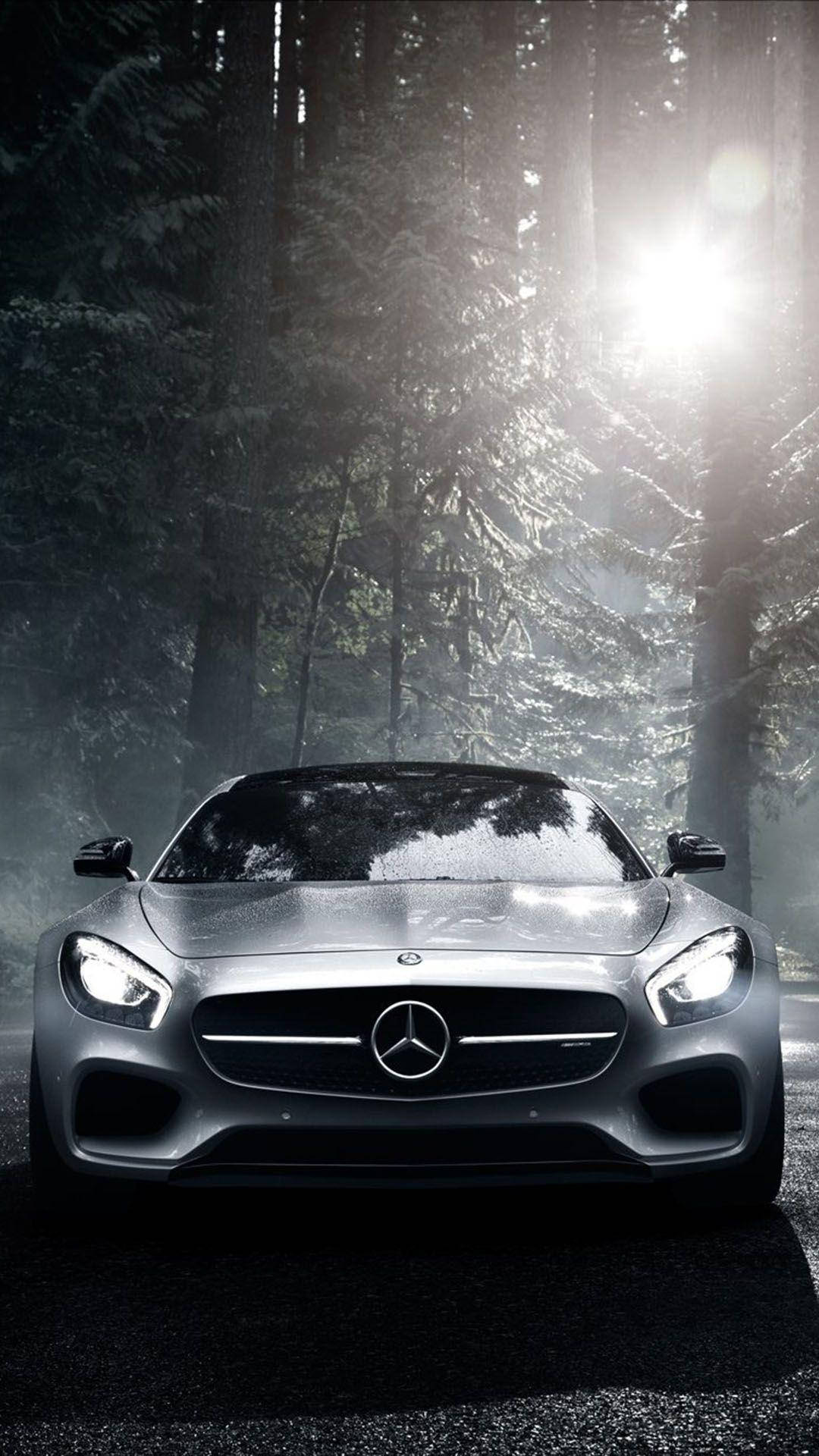 mercedes iPhone 桌布 壁紙 — 一輛時尚的銀色梅賽德斯跑車在高聳松樹間戲劇性的森林光線下閃閃發光。