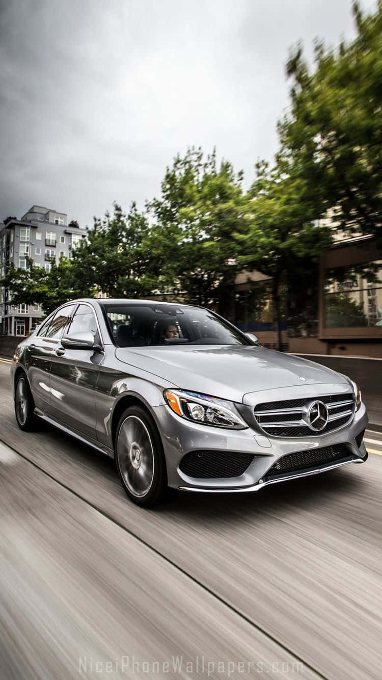 Mercedes 桌布 壁紙 — 一輛時尚的銀色梅賽德斯轎車在城市的街道上飛馳，帶有動態模糊效果，道路兩旁綠樹成蔭。