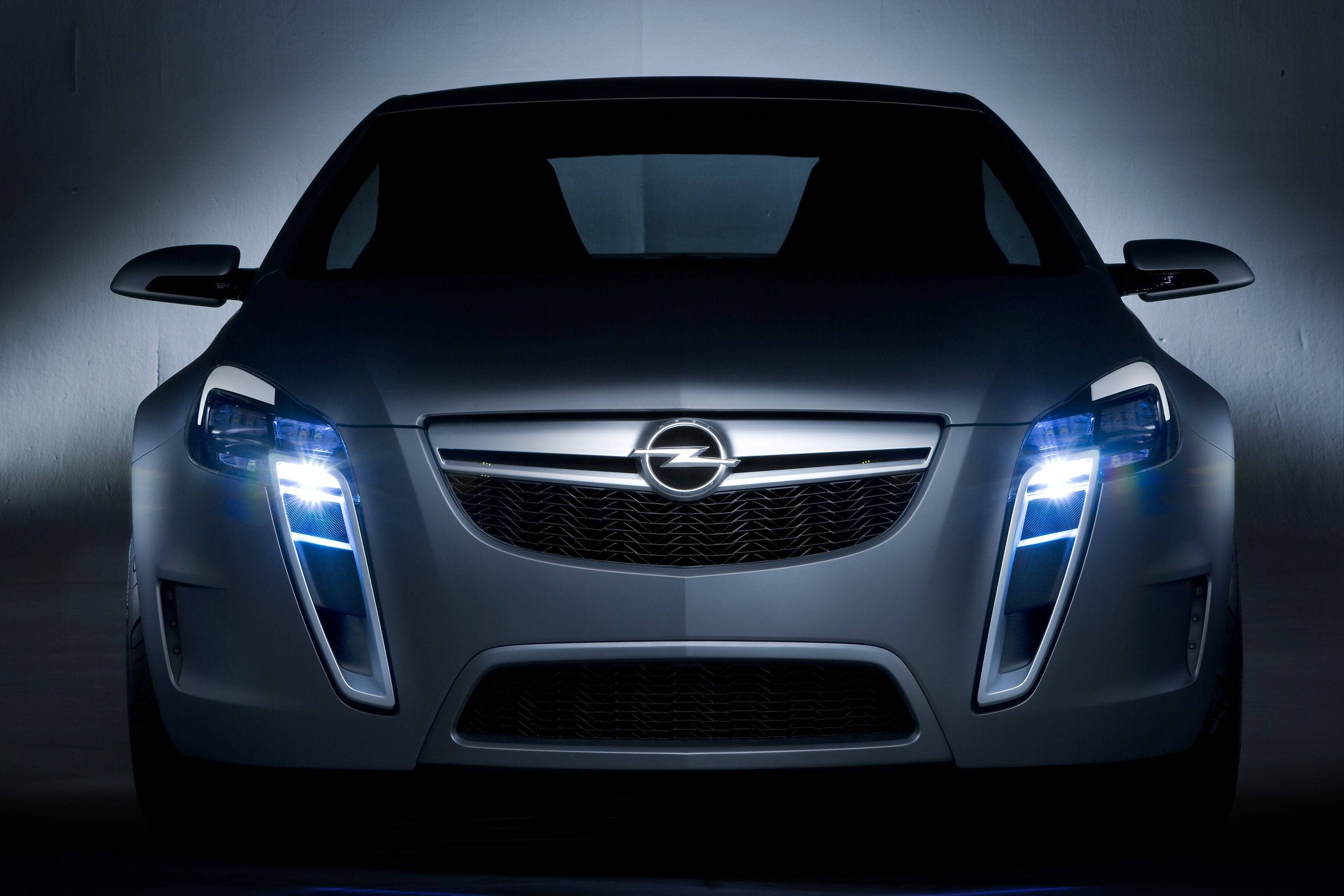 Opel 桌布 壁紙 — 一輛時尚的銀色歐寶概念車，帶有發光的藍色頭燈，在黑暗的攝影棚環境中向前凝視。