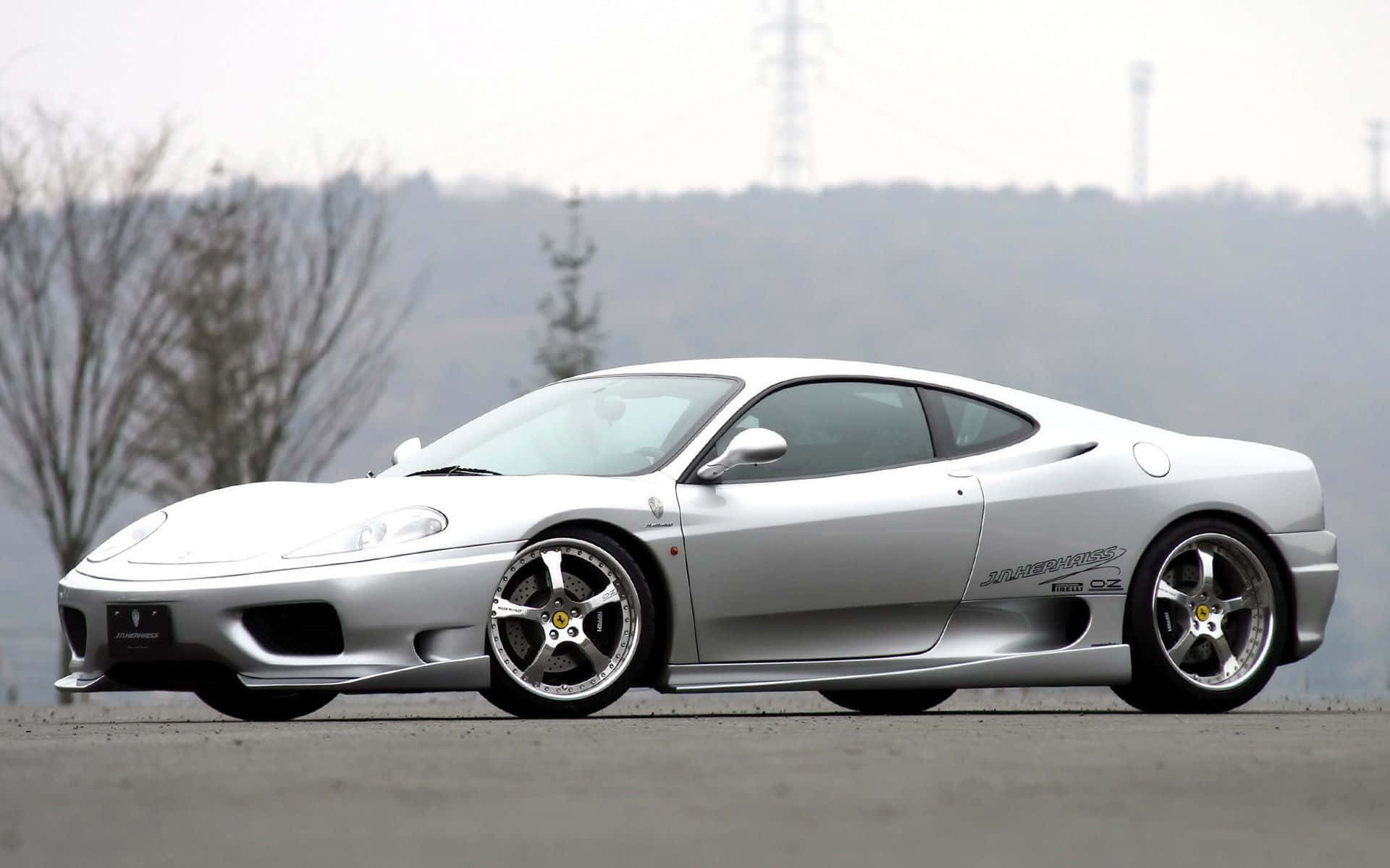 Ferrari 360 Modena 桌布 壁紙 — 一輛時尚的銀色法拉利 360 Modena 跑車停放在開闊的瀝青停車場上，背景有霧氣籠罩的禿樹和山丘。