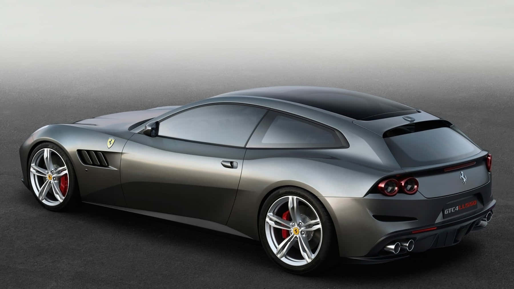 Ferrari Gtc4lusso 桌布 壁紙 — 一輛時尚的銀色法拉利 GTC4Lusso 跑車，配備紅色制動卡鉗和雙排氣管，從後方四分之三角度拍攝，背景為簡約灰色攝影棚。