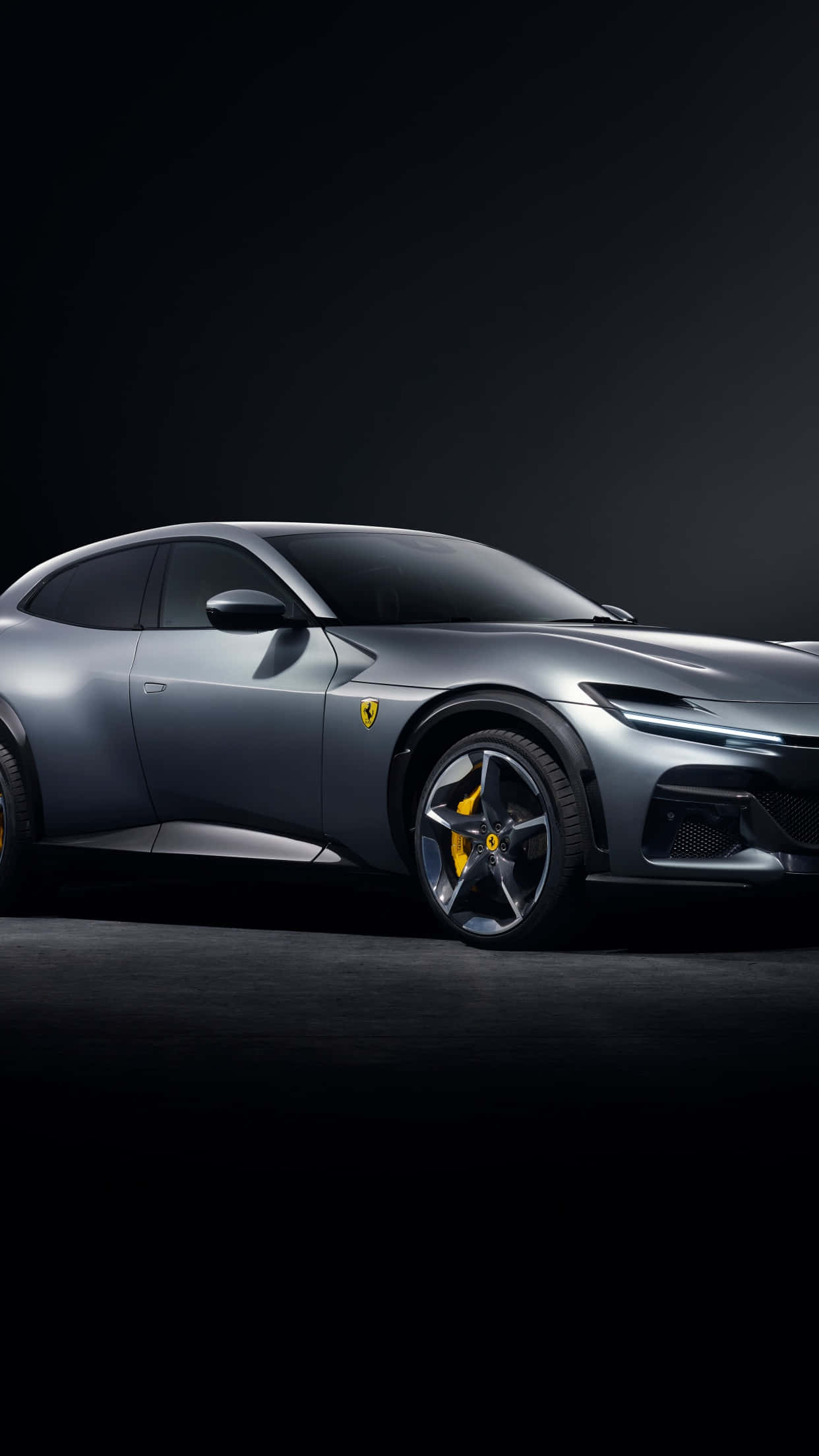 Ferrari iPhone 桌布 壁紙 — 一輛時尚的銀色法拉利 Purosangue SUV 在攝影棚燈光下，以黑色背景和黃色制動卡鉗閃耀光芒。