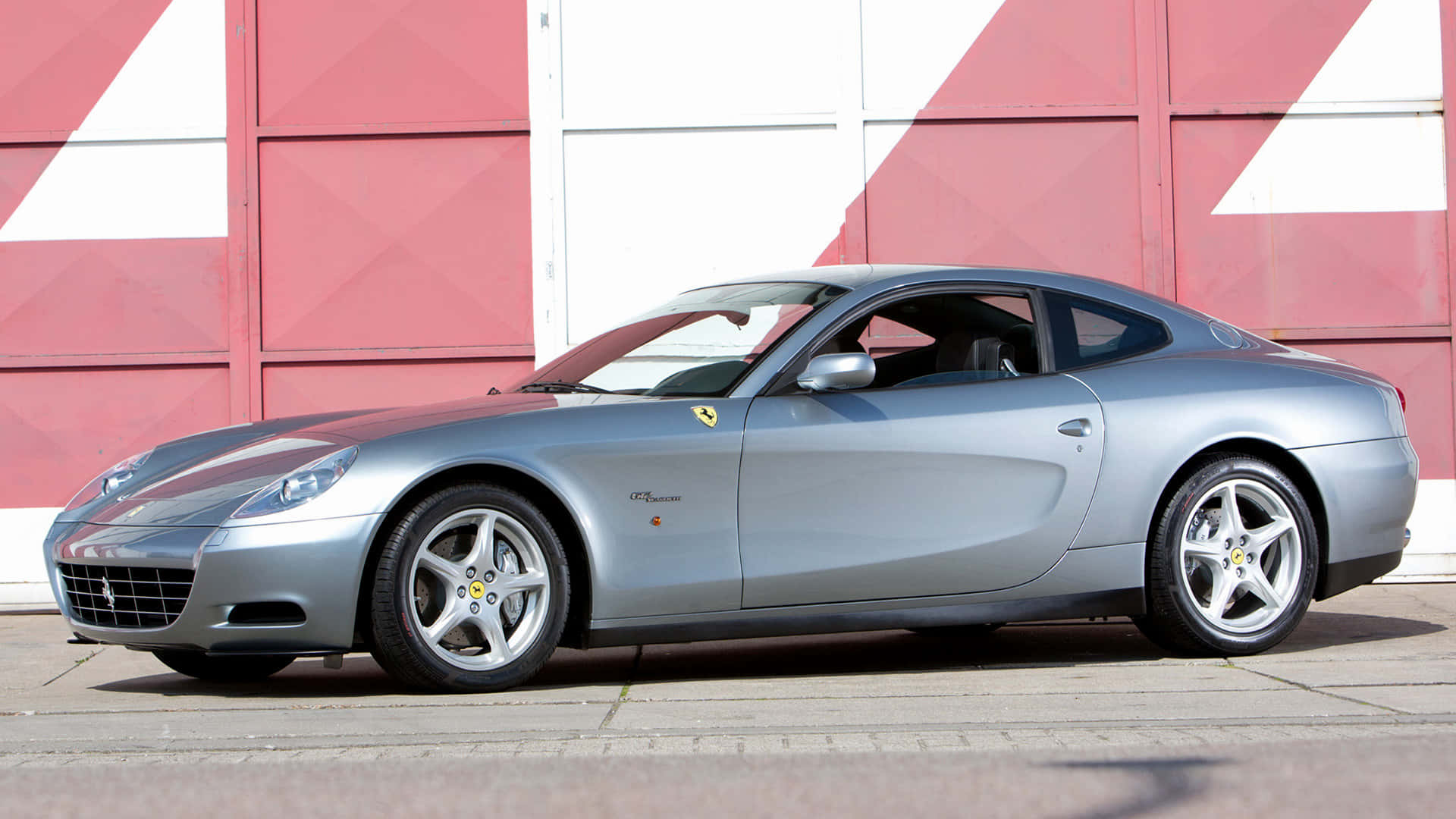 Ferrari 612 Scaglietti 桌布 壁紙 — 一輛時尚的銀色法拉利612 Superamerica停放在紅白條紋車庫門前。