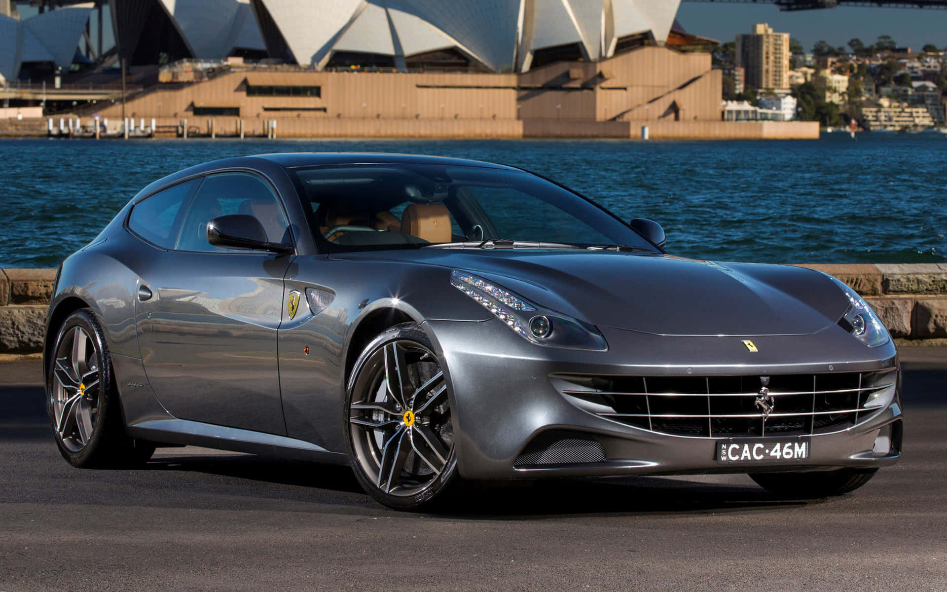 Ferrari Ff 桌布 壁紙 — 一輛時尚的銀色法拉利FF停在水邊，背景是雪梨歌劇院，在明亮的日光下。