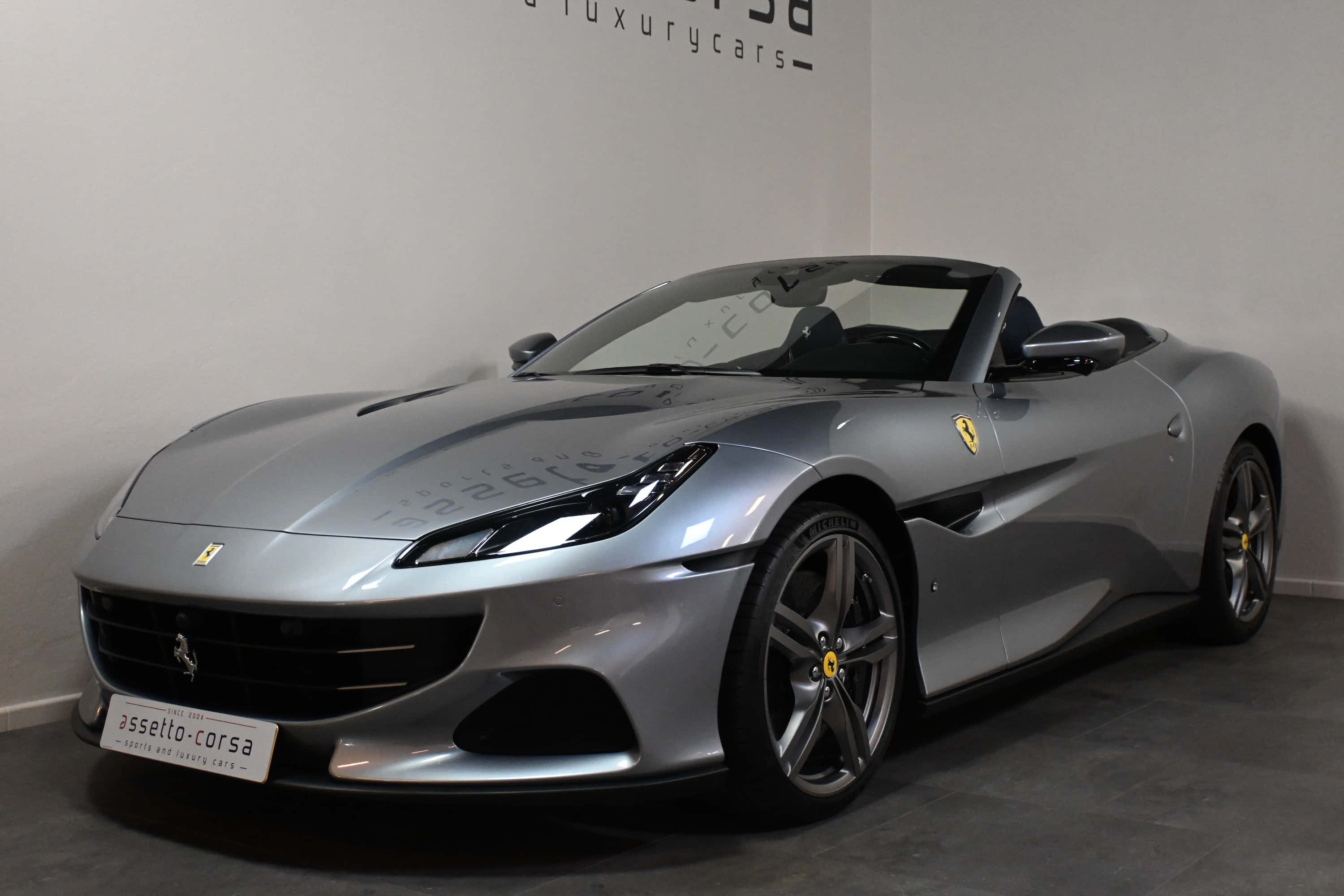 Ferrari Portofino 桌布 壁紙 — 一輛時尚的銀色法拉利敞篷車停放在室內，具有拋光曲線和黃色躍馬標誌。