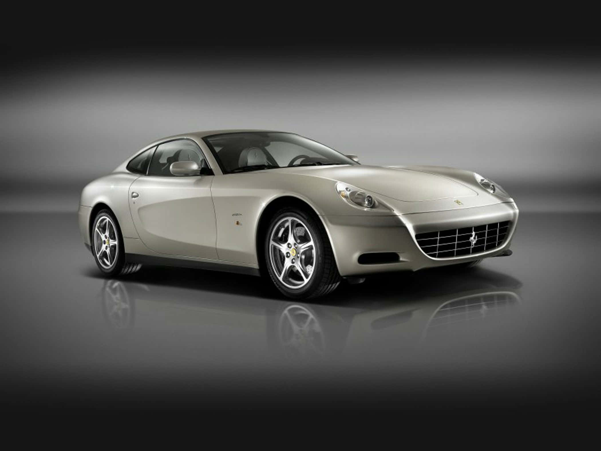 Ferrari 612 Scaglietti 桌布 壁紙 — 一輛時尚的銀色法拉利跑車在攝影棚燈光下，在反光的深色地板上閃閃發光。