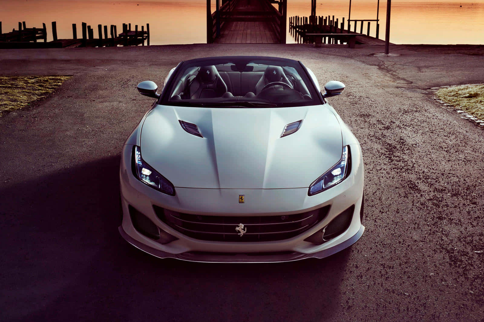 Ferrari Portofino 桌布 壁紙 — 一輛時尚的銀色法拉利跑車在日落時分面向前方停在碎石路上，背景是木製碼頭。
